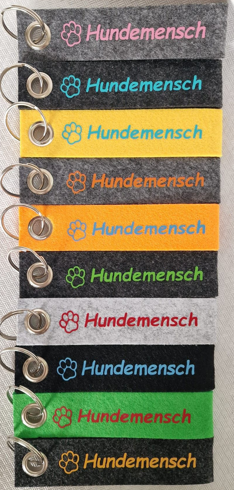 Schlüsselanhänger in verschiedenen Farben mit dem Schriftzug „Hundemensch“ und einem Pfotenabdrucksymbol.