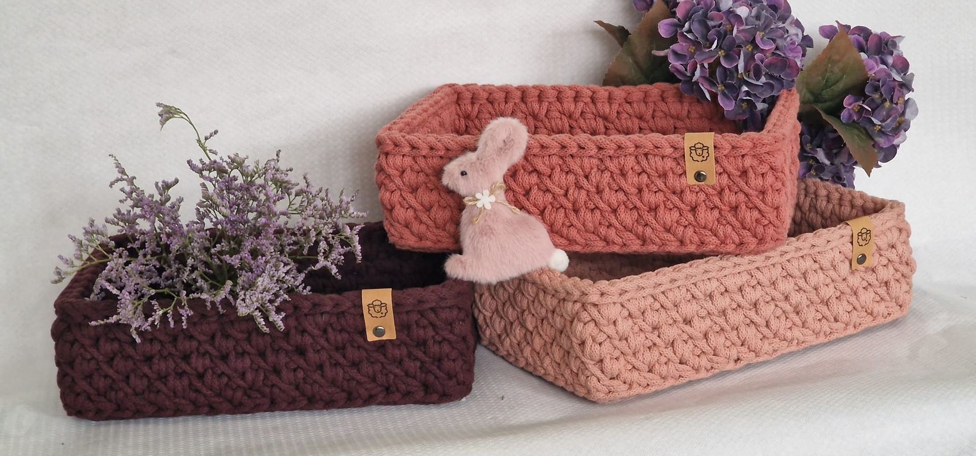 Drei gehäkelte Körbe in verschiedenen Farben mit Blumen und einem Hasen.