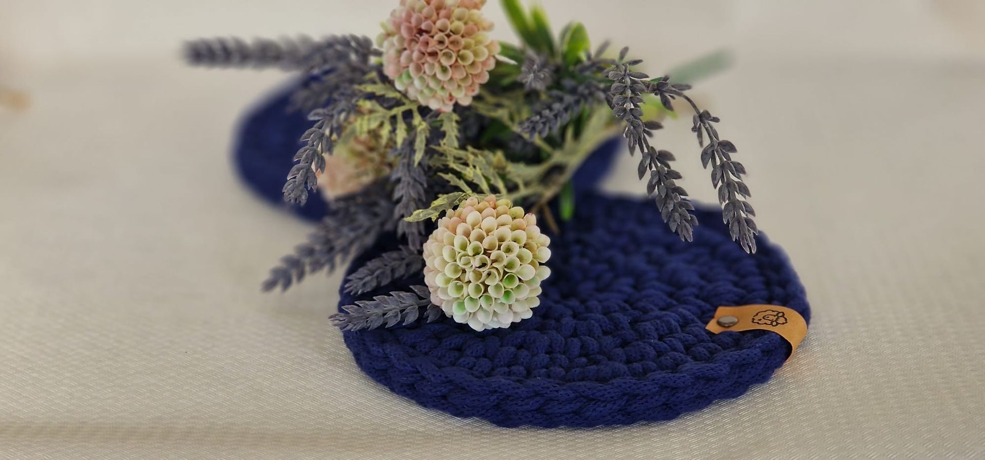 Blaue, gehäkelte Untersetzer, verziert mit Lavendel und runden Blütenknospen auf hellem Hintergrund.