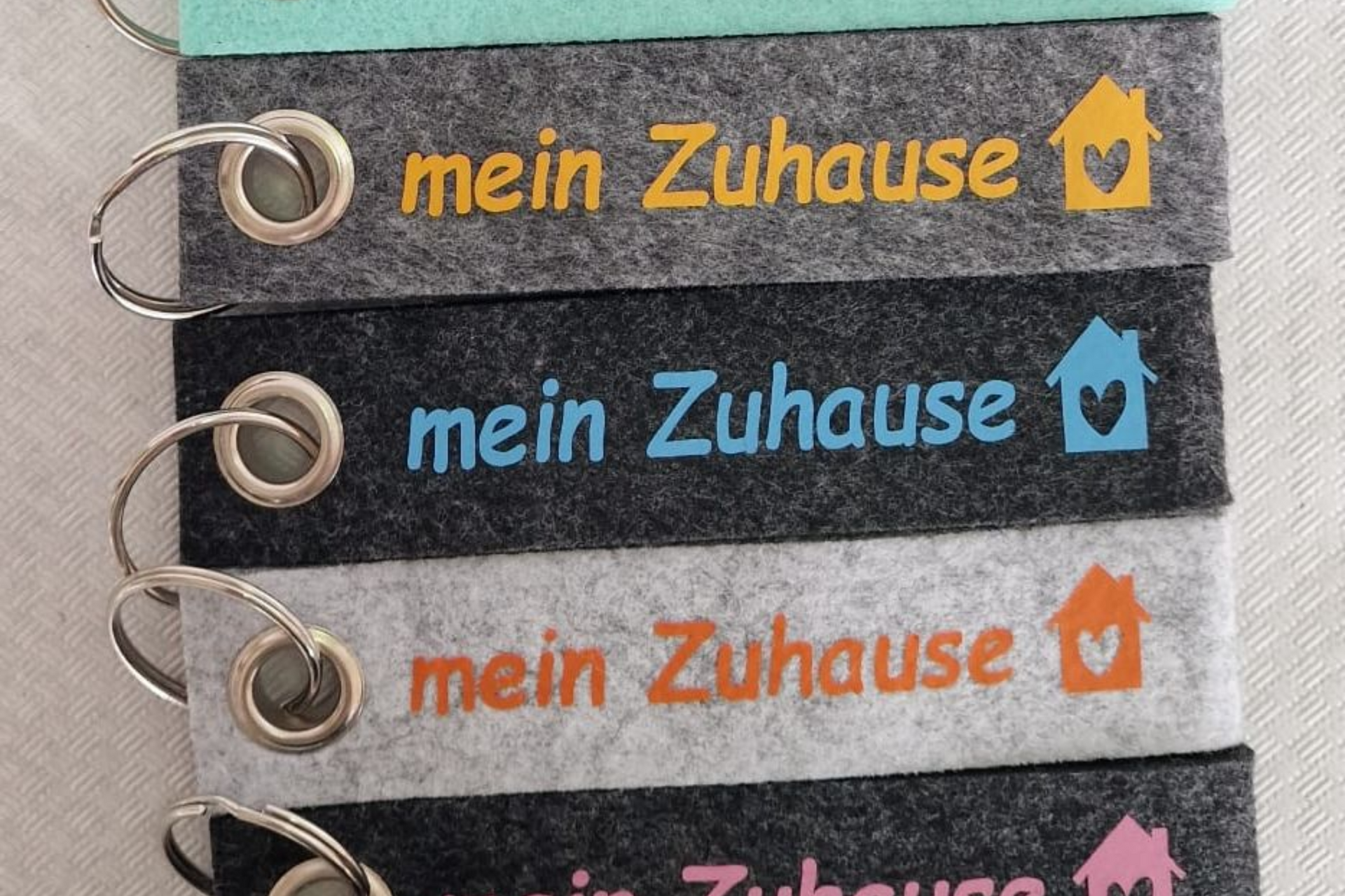 Schlüsselanhänger mit dem Schriftzug „mein Zuhause“ und Haus-Symbolen in verschiedenen Farben.