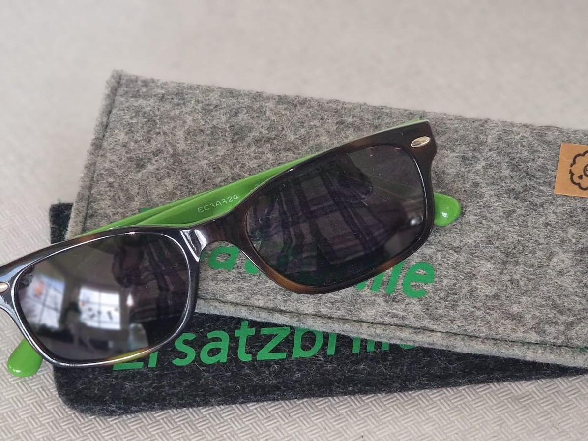 Sonnenbrille mit braunem Gestell und grünen Bügeln in einem grauen Filzetui.