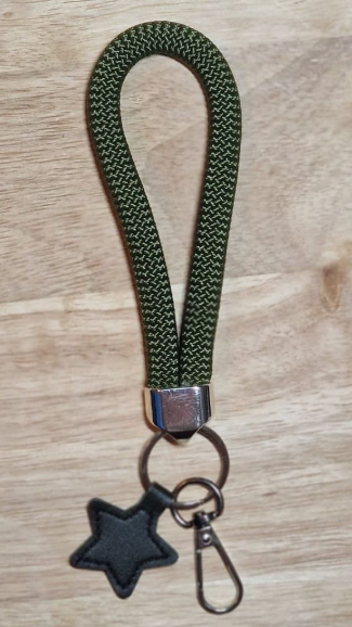Olivgrüner, geflochtener Schlüsselanhänger mit Armband, Sternanhänger und Karabinerverschluss auf Holzgrund.
