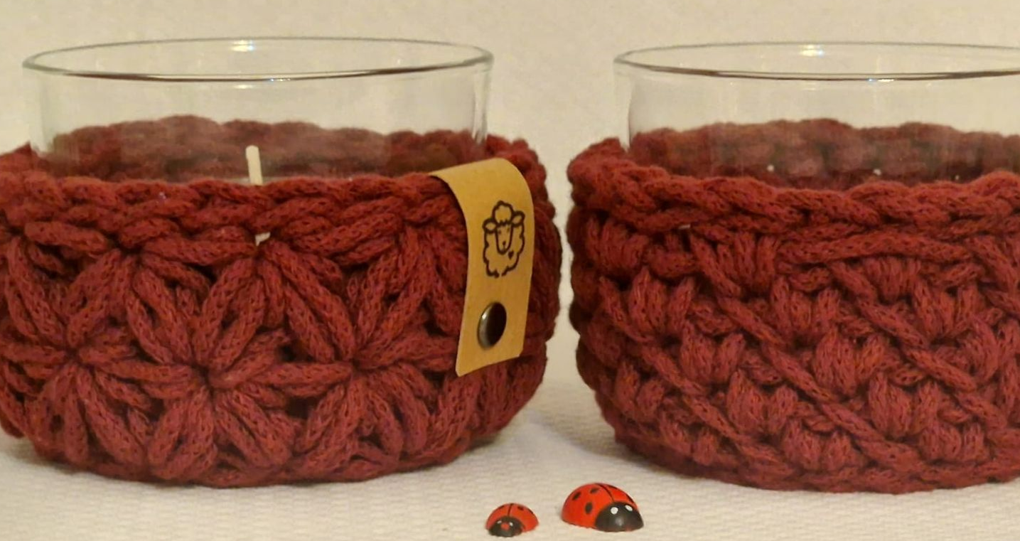 Zwei gläserne Kerzenhalter mit bordeauxroten, gehäkelten Überzügen.