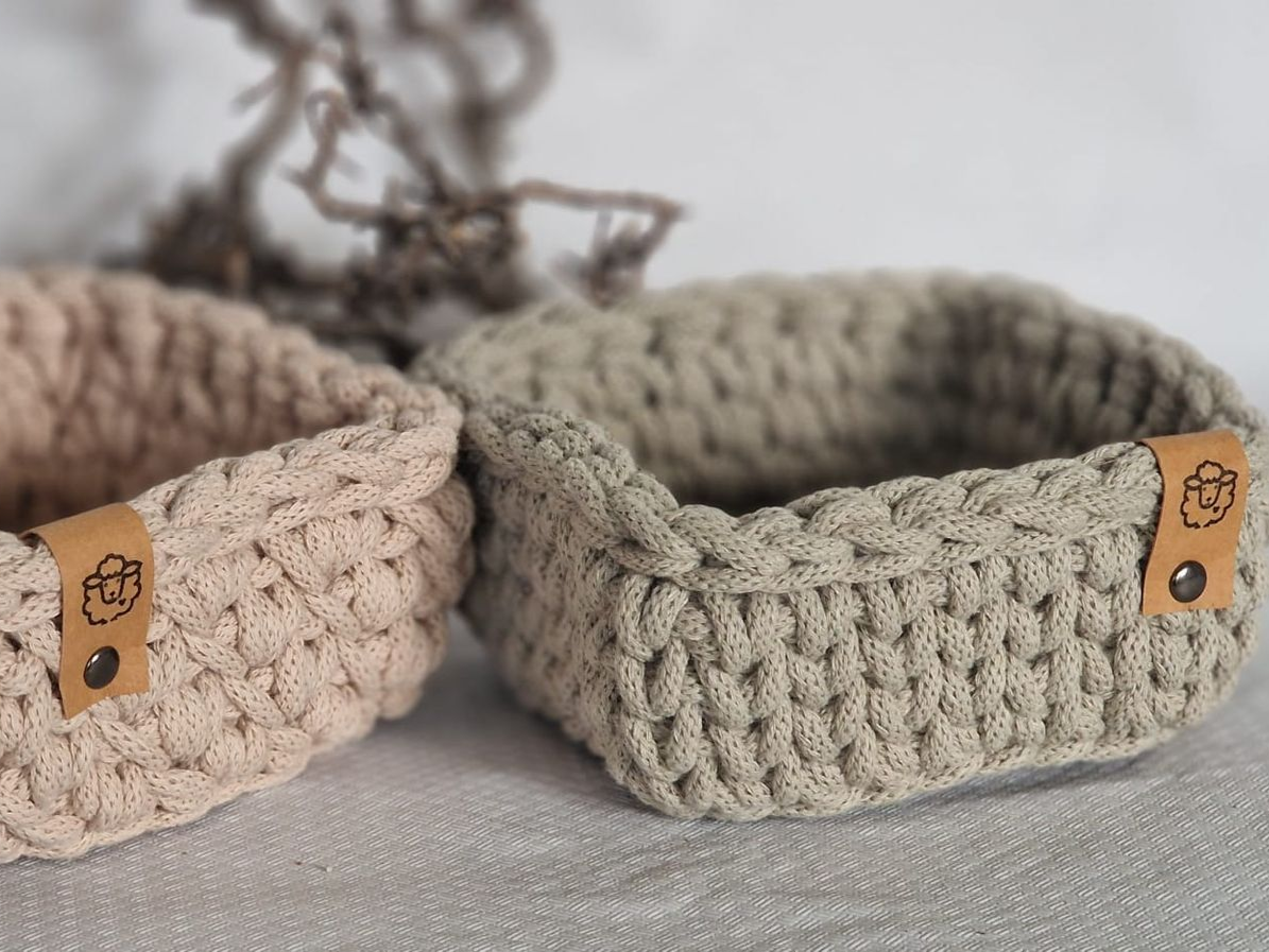 Zwei gehäkelte Körbe in Beige und Grau mit Lederanhängern.