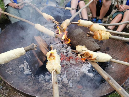Pfadfinder sitzen gemeinsam am Lagerfeuer und backen Stockbrot