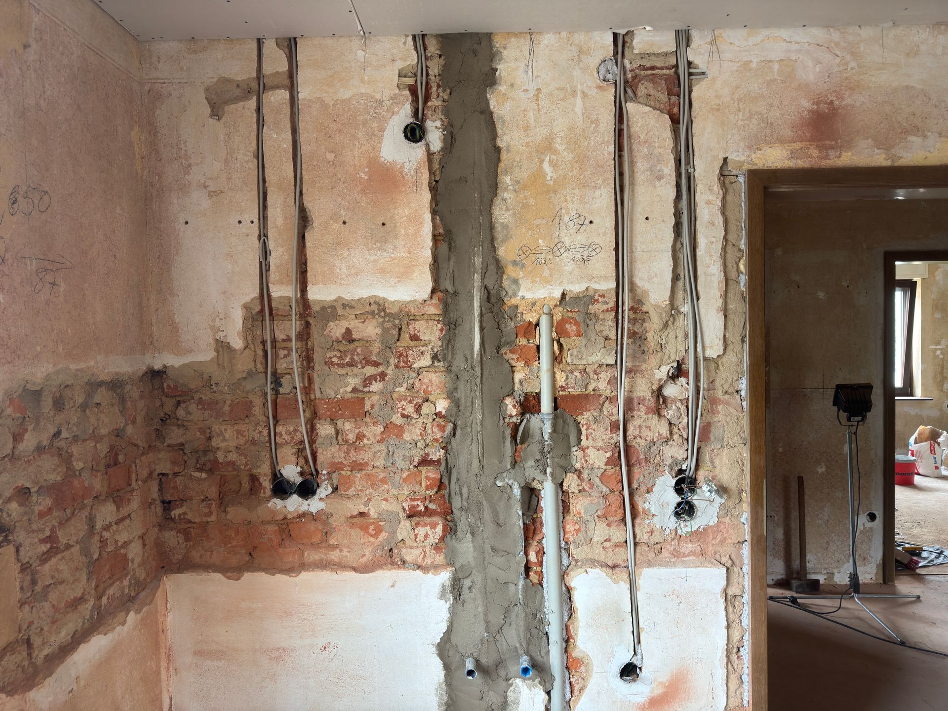 Beschädigte Wand mit freiliegenden Ziegeln, Stromleitungen und einer groben Putzstelle in einem Zimmer