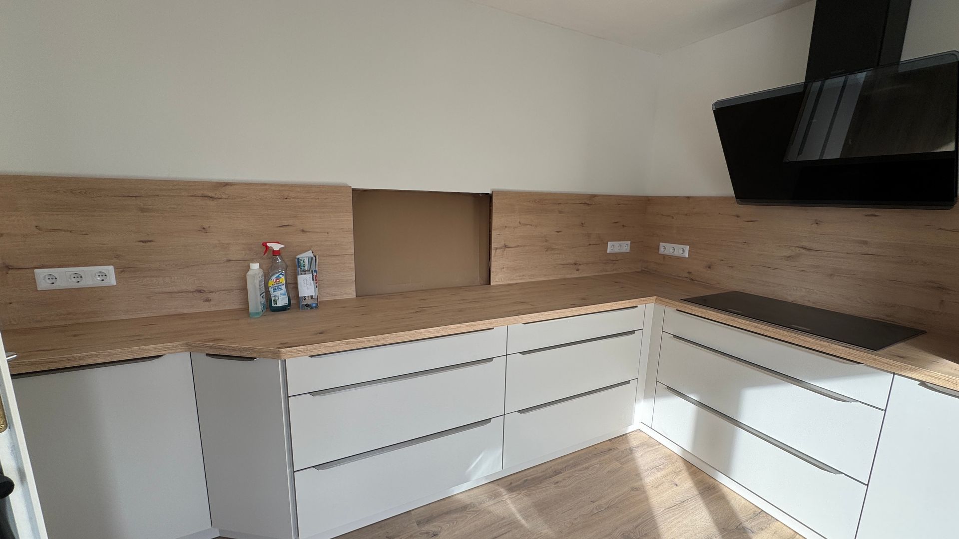 Moderne Küche mit weißen Schränken, Holzrückwand, schwarzer Dunstabzugshaube und beiger Arbeitsplatte