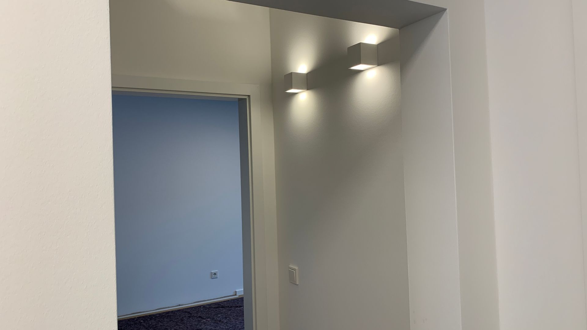 Fluröffnung mit eingelassenen Deckenleuchten und Tür zu einem blau gestrichenen Zimmer