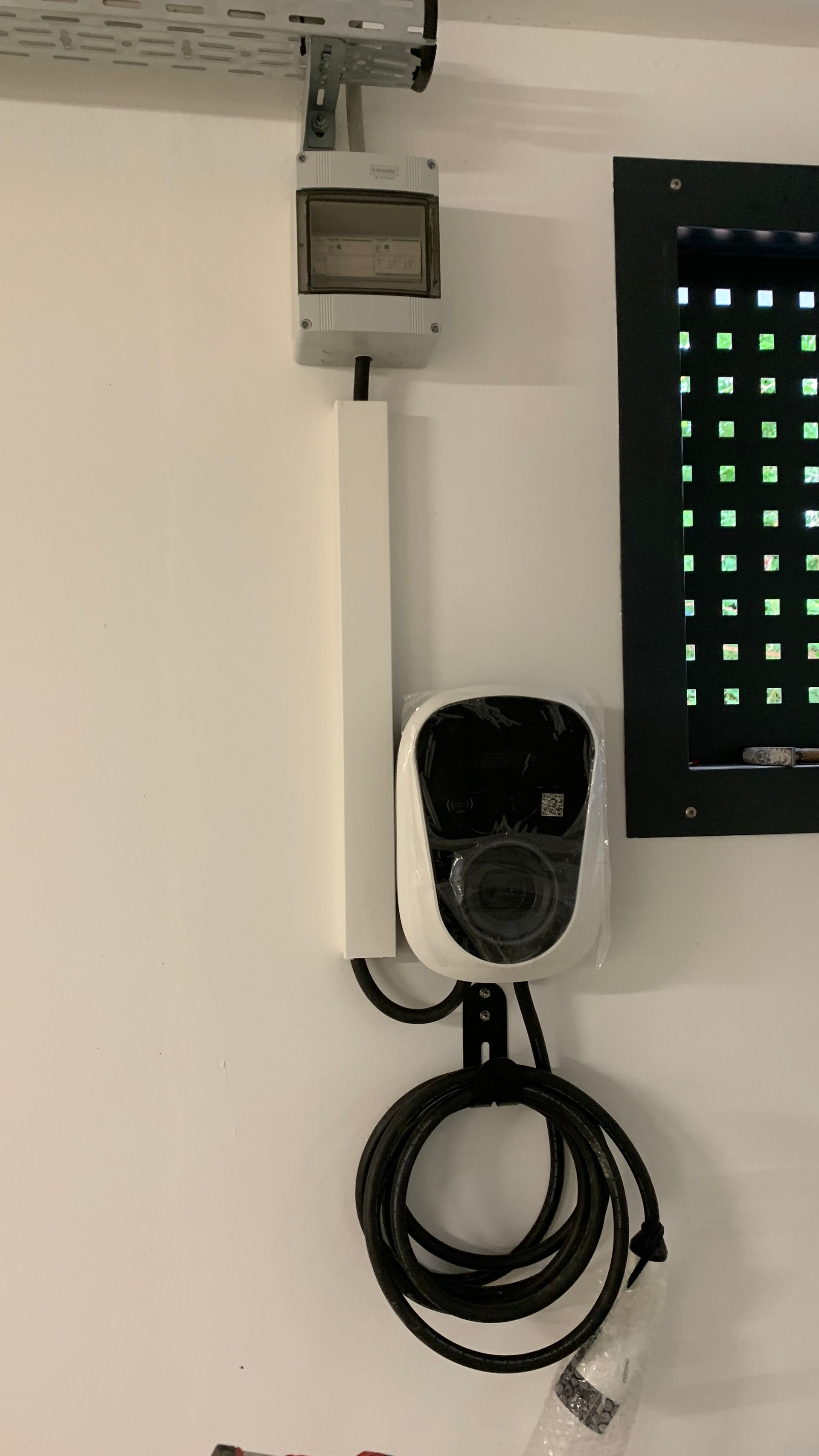 Wandmontierte Sicherheitskamera mit aufgerolltem Kabel unter einer an der Decke montierten Anschlussdose und schwarzer Lüftungsblende.