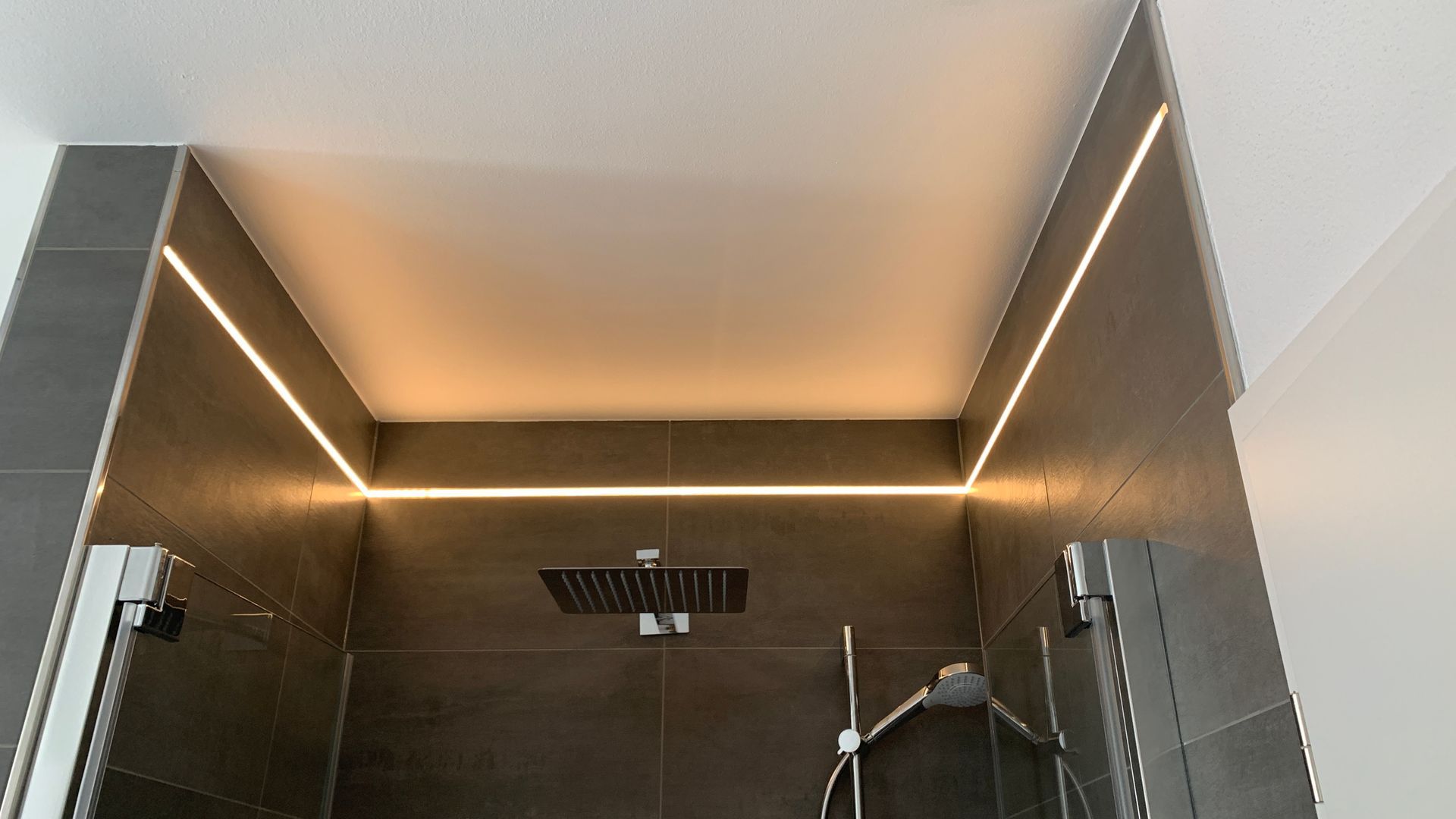 Moderne, ebenerdige Dusche mit dunkel gefliesten Wänden und warmem LED-Lichtband