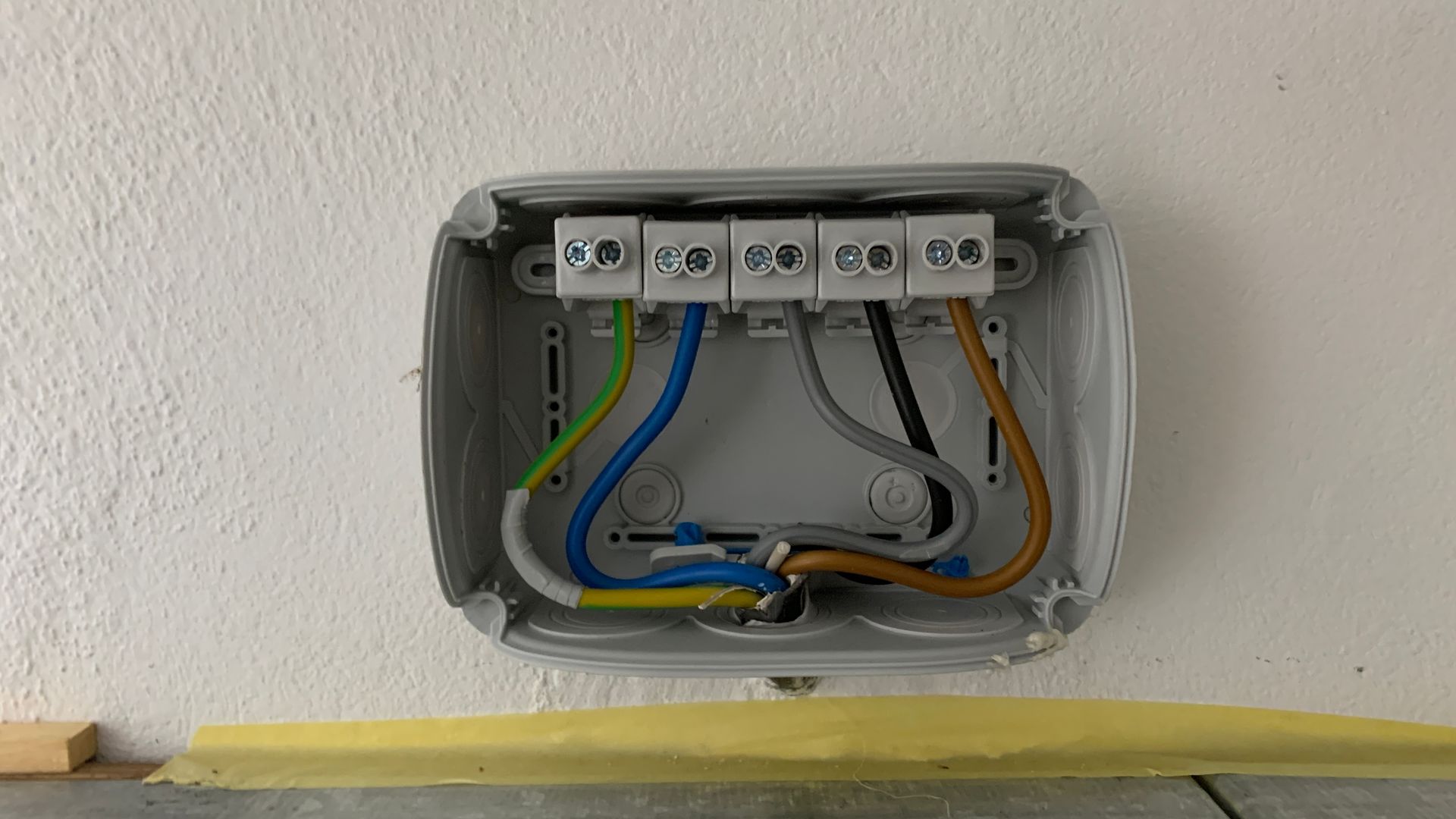Offene elektrische Anschlussdose mit freiliegenden farbigen Drähten an einer Wand.