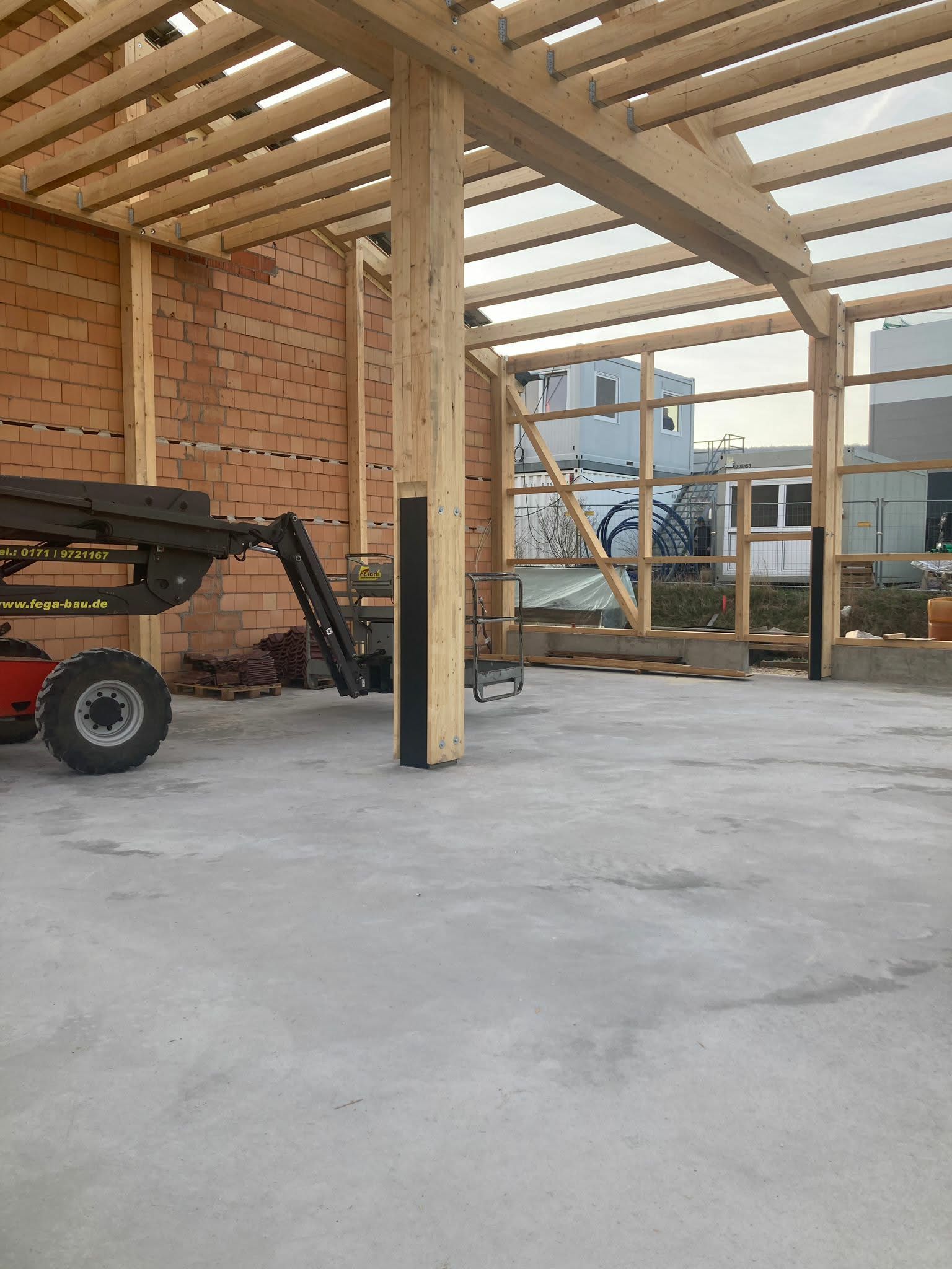 Ein unfertiges Gebäude mit freiliegenden Ziegelwänden, Holzbalken, einem Betonboden und schweren Maschinen im Inneren.