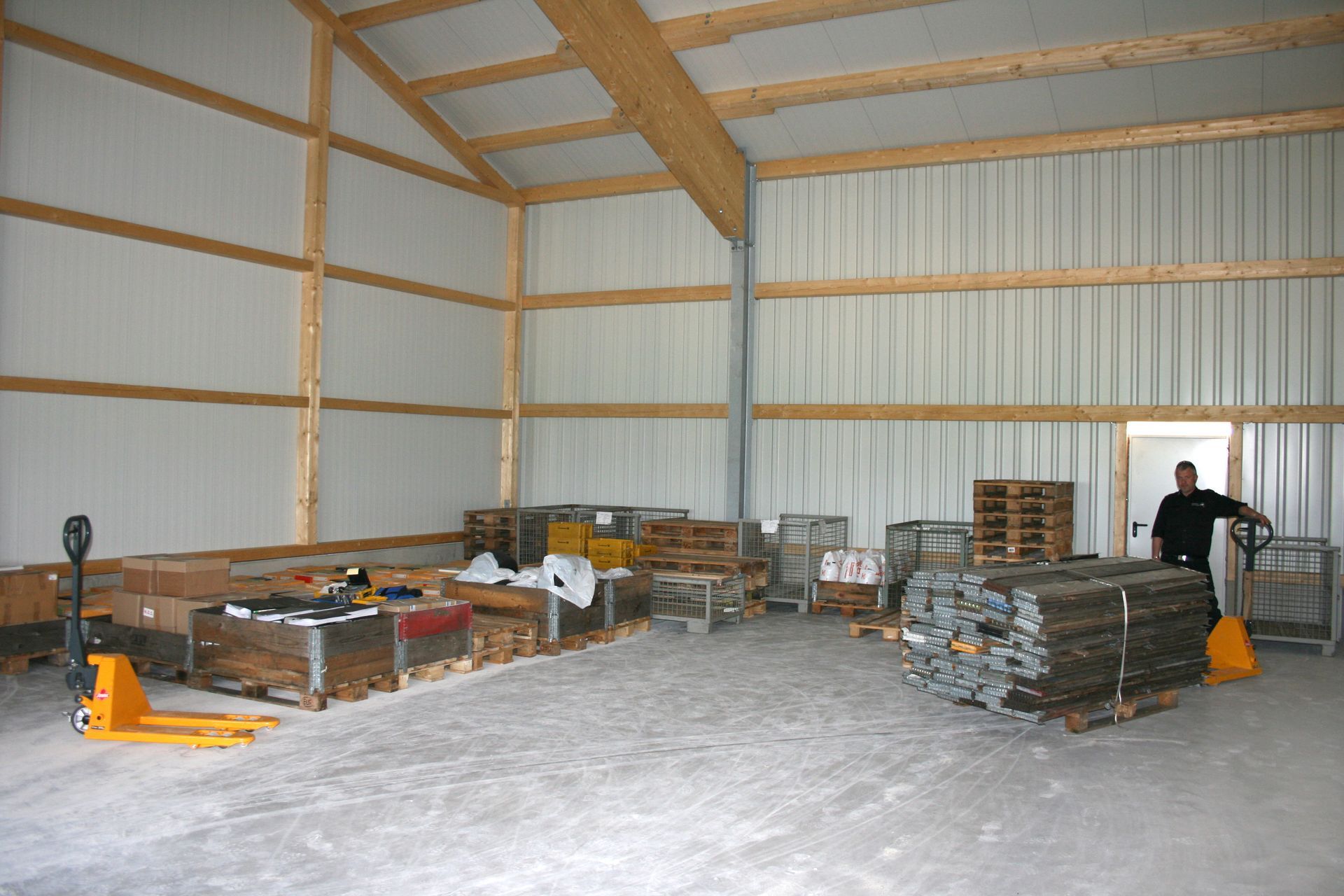 Eine geräumige Lagerhalle mit Holzrahmen, gestapelten Paletten, Ausrüstung und einer Person, die in der Nähe einer offenen Tür steht.
Privatarchiv Martin Heinze