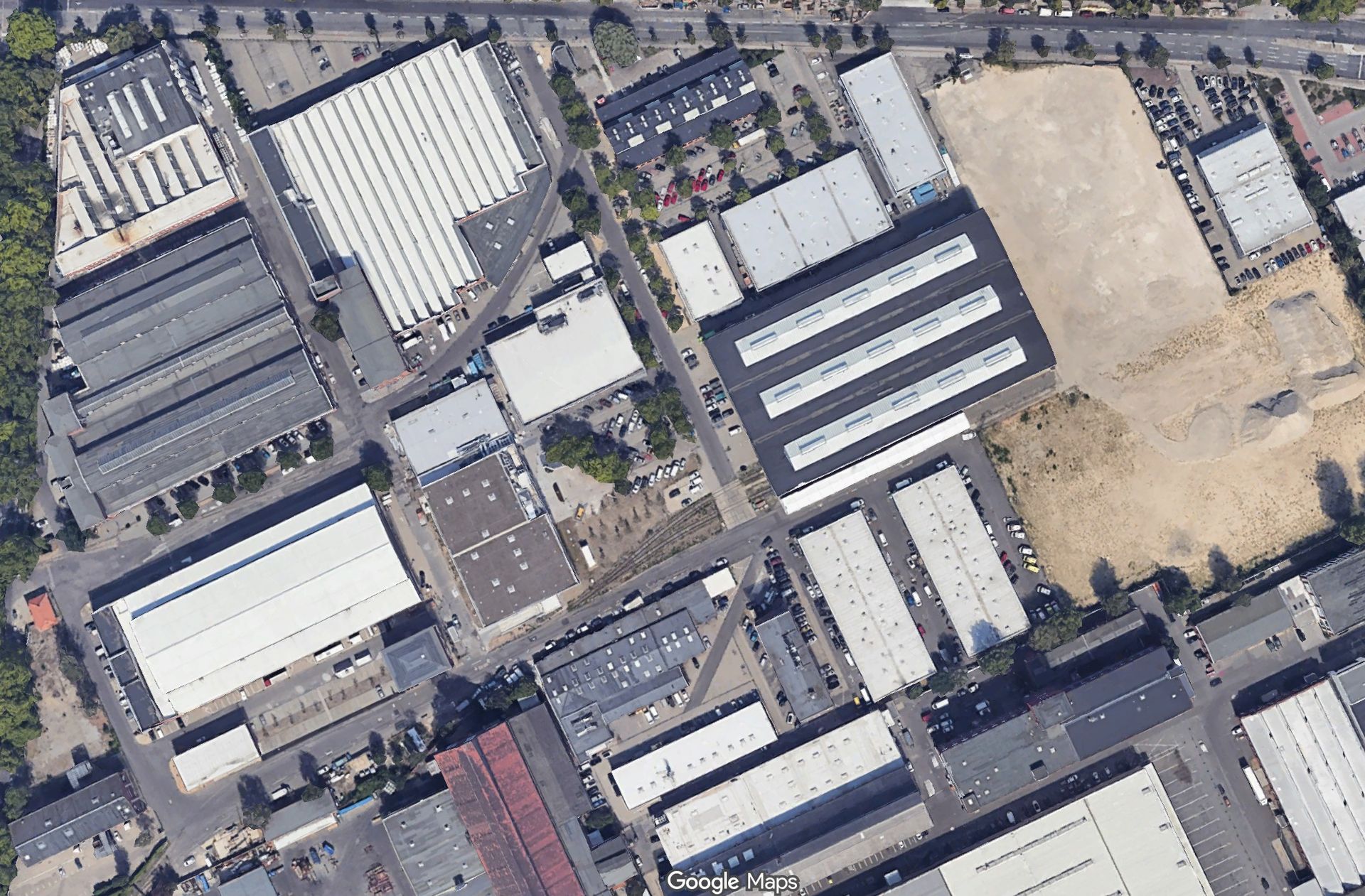 Luftaufnahme eines Industriegebiets mit Lagerhallen, Straßen und unbebauten Grundstücken.