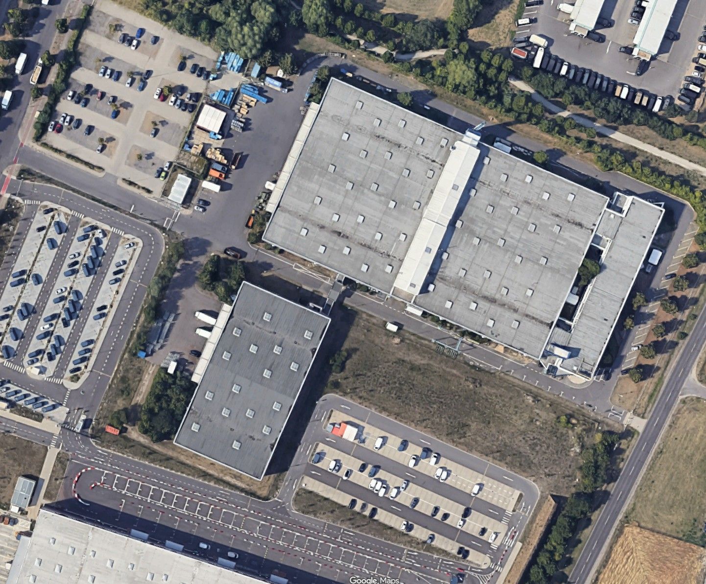 Luftaufnahme von großen Industriegebäuden, Parkplätzen und umliegenden Straßen.