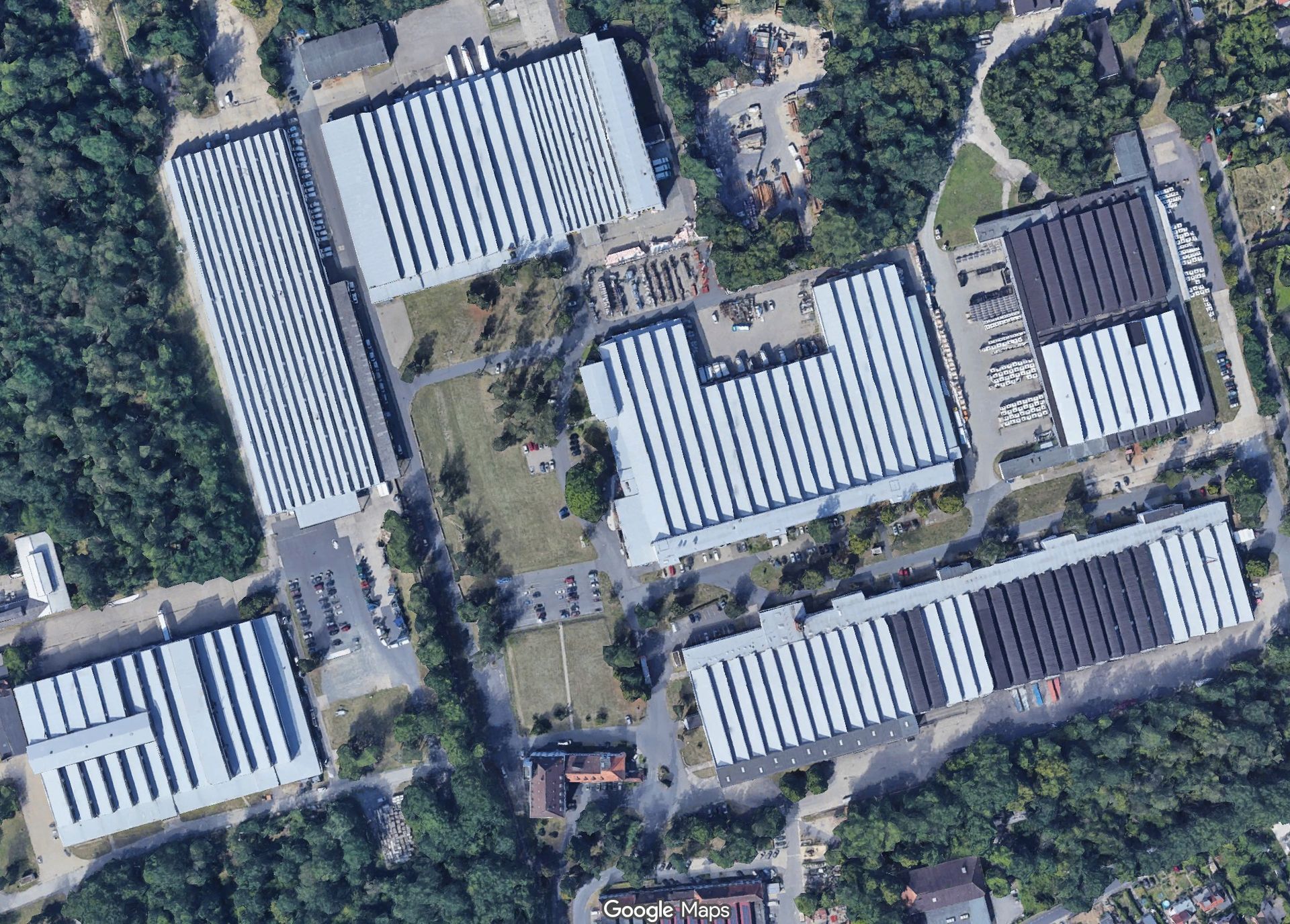 Luftaufnahme eines Lagerhauskomplexes mit mehreren langen, weiß gedeckten Gebäuden, die von Bäumen umgeben sind.