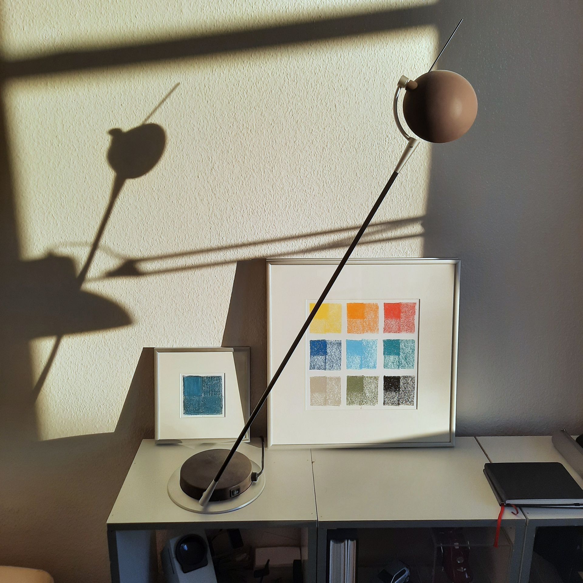 Zwei Bilder auf einem Sideboard in der Sonne und mit Schatten von zwei filigranen Leuchten.