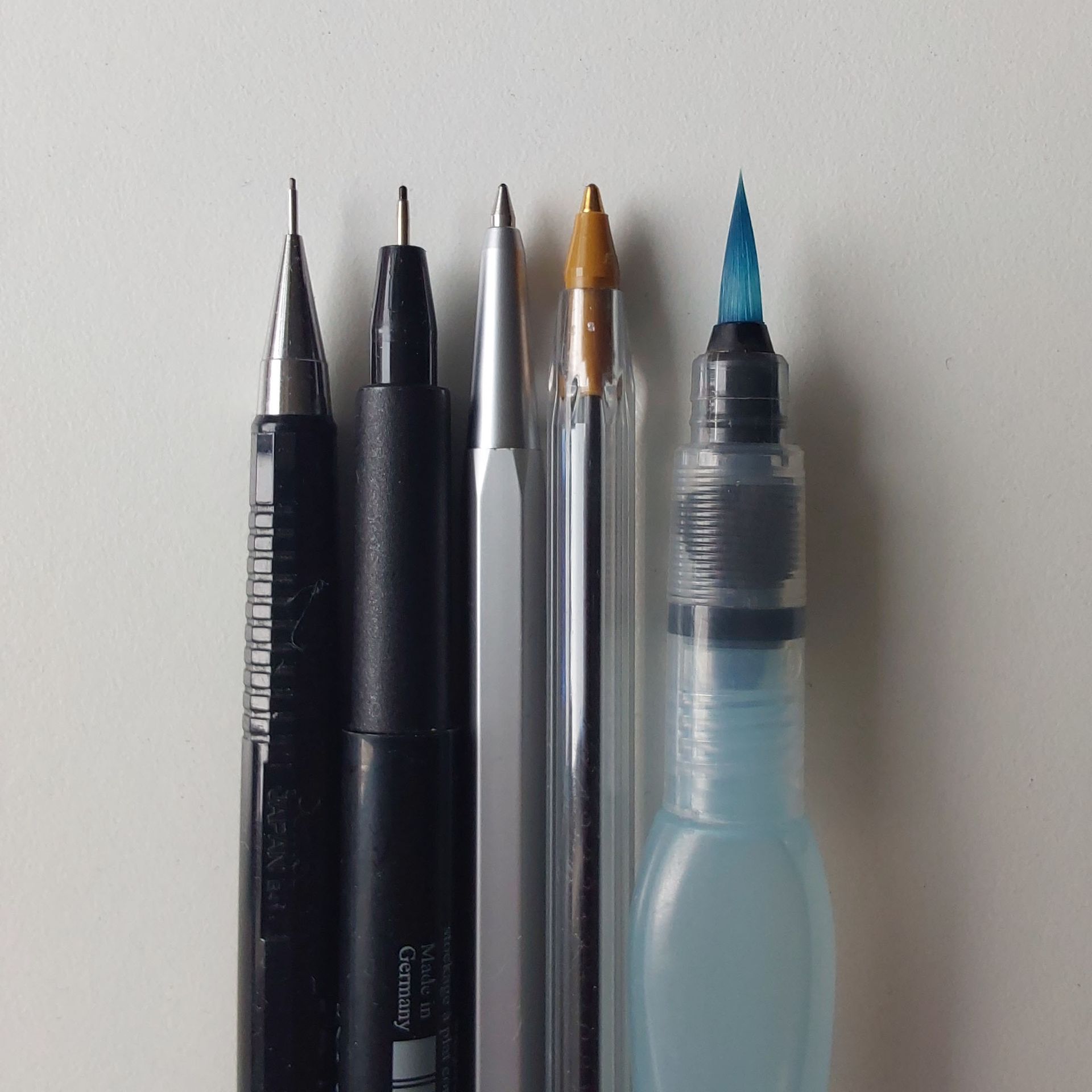 Spitzen von fünf Stiften: Druckbleistift, Filzstift, zwei Kugelschreiber, und die Pinselspitze eines Wassertankpinsels.