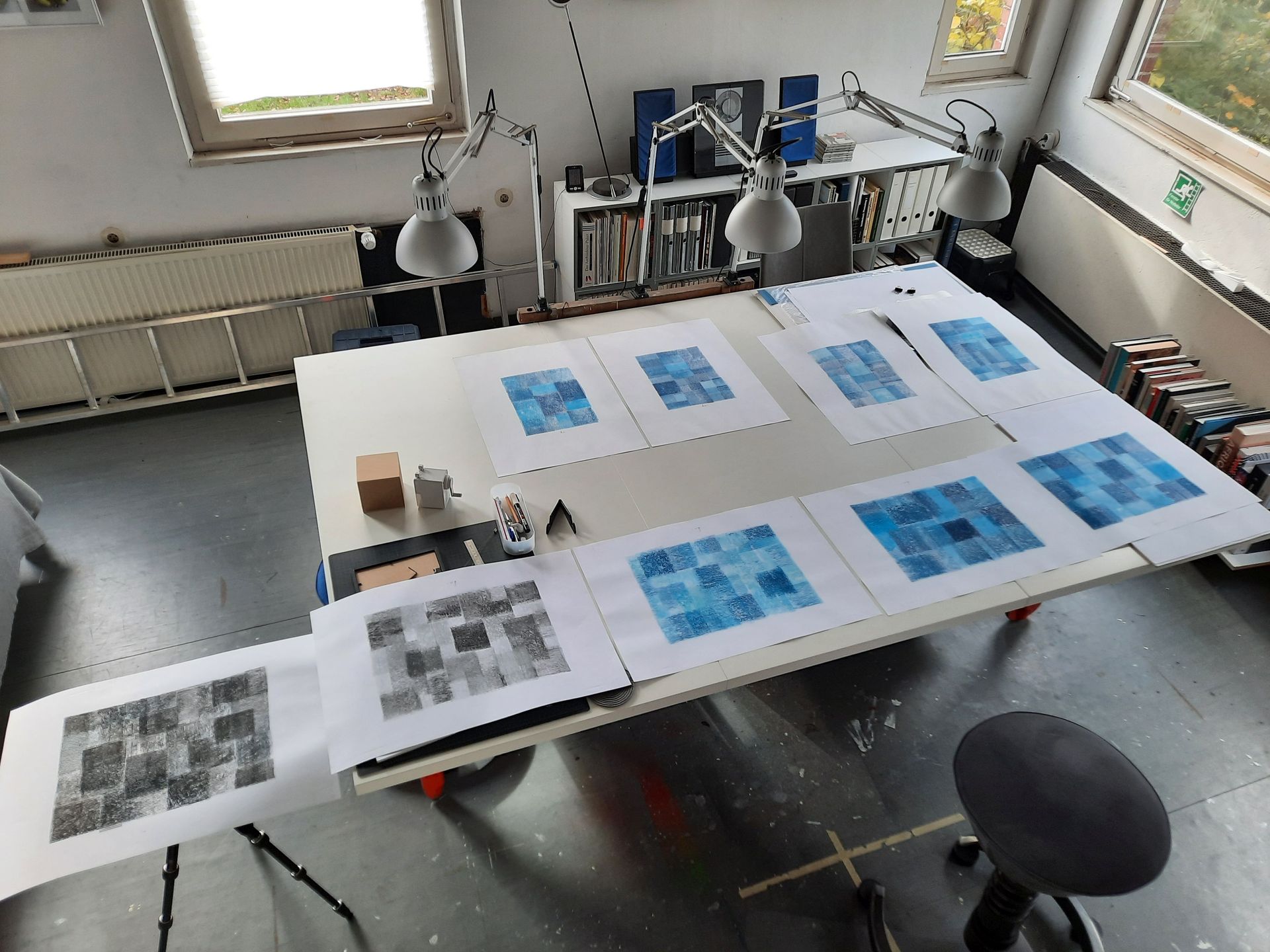 Schrägaufsicht auf einen Ateliertisch mit 5 Bildern nebeneinander im Querformat und 4 Bildern im Hochformat.