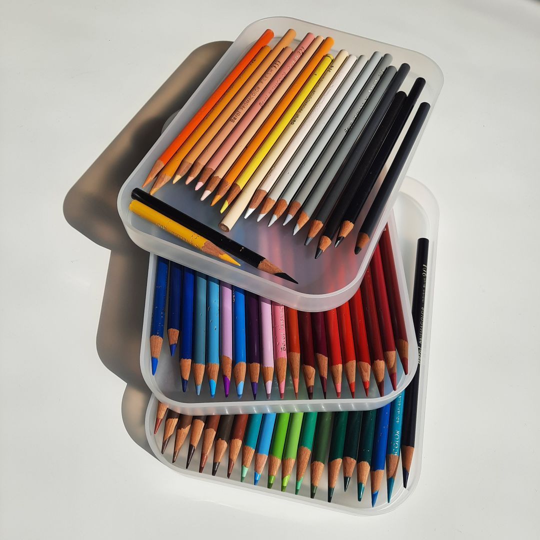 Drei gestapelte flache Kunststoffkästen mit Buntstiften.