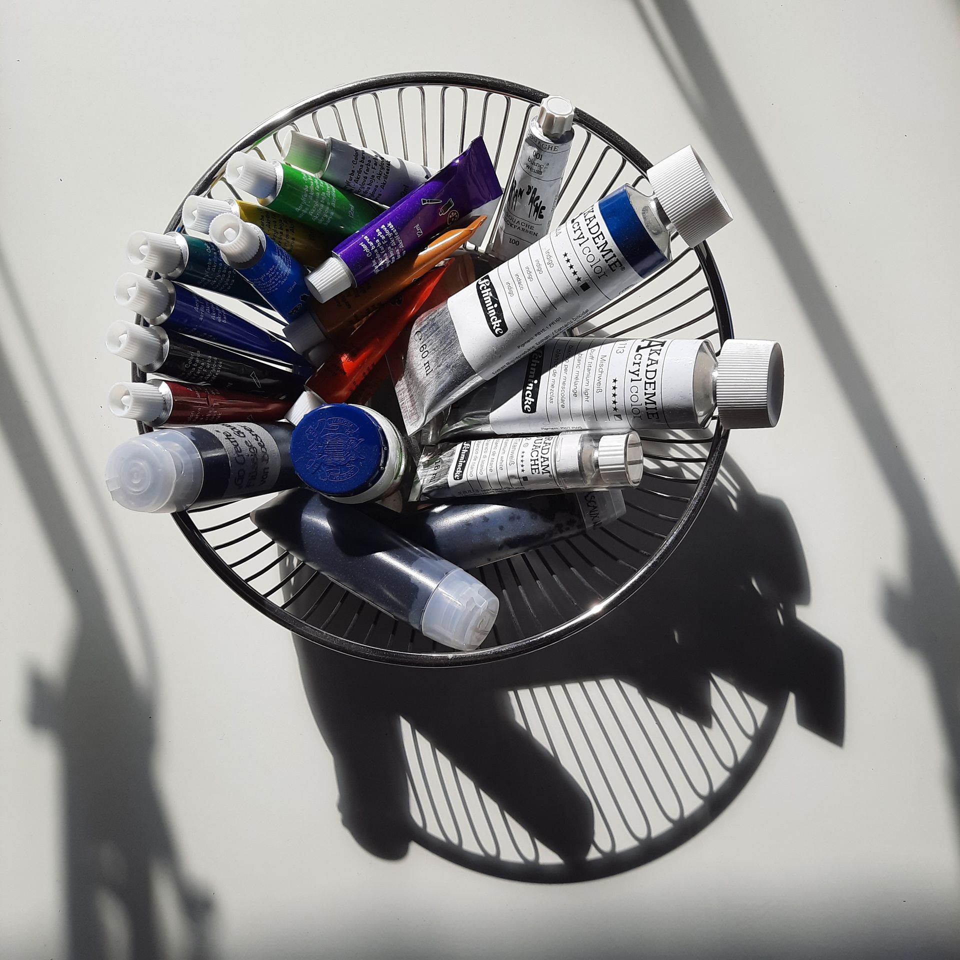 Runde Schale aus Metalldrähten, in der Farbtuben liegen: Acrylfarbe und Aquarellfarbe.