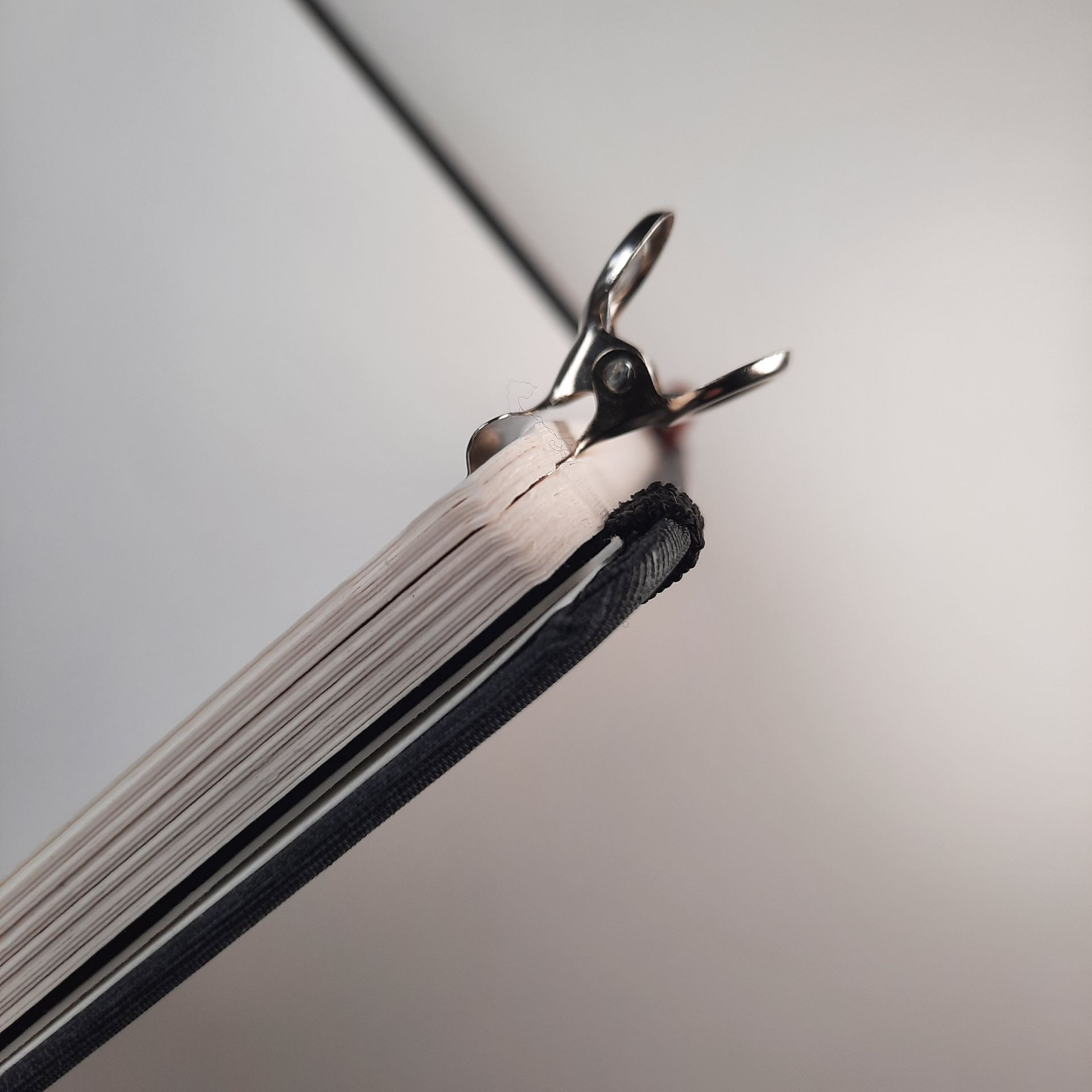 Seitenansicht eines Skizzenbuches, in dem einige Seiten mit einer einseitig platten Metallklammer zusammengehalten werden.