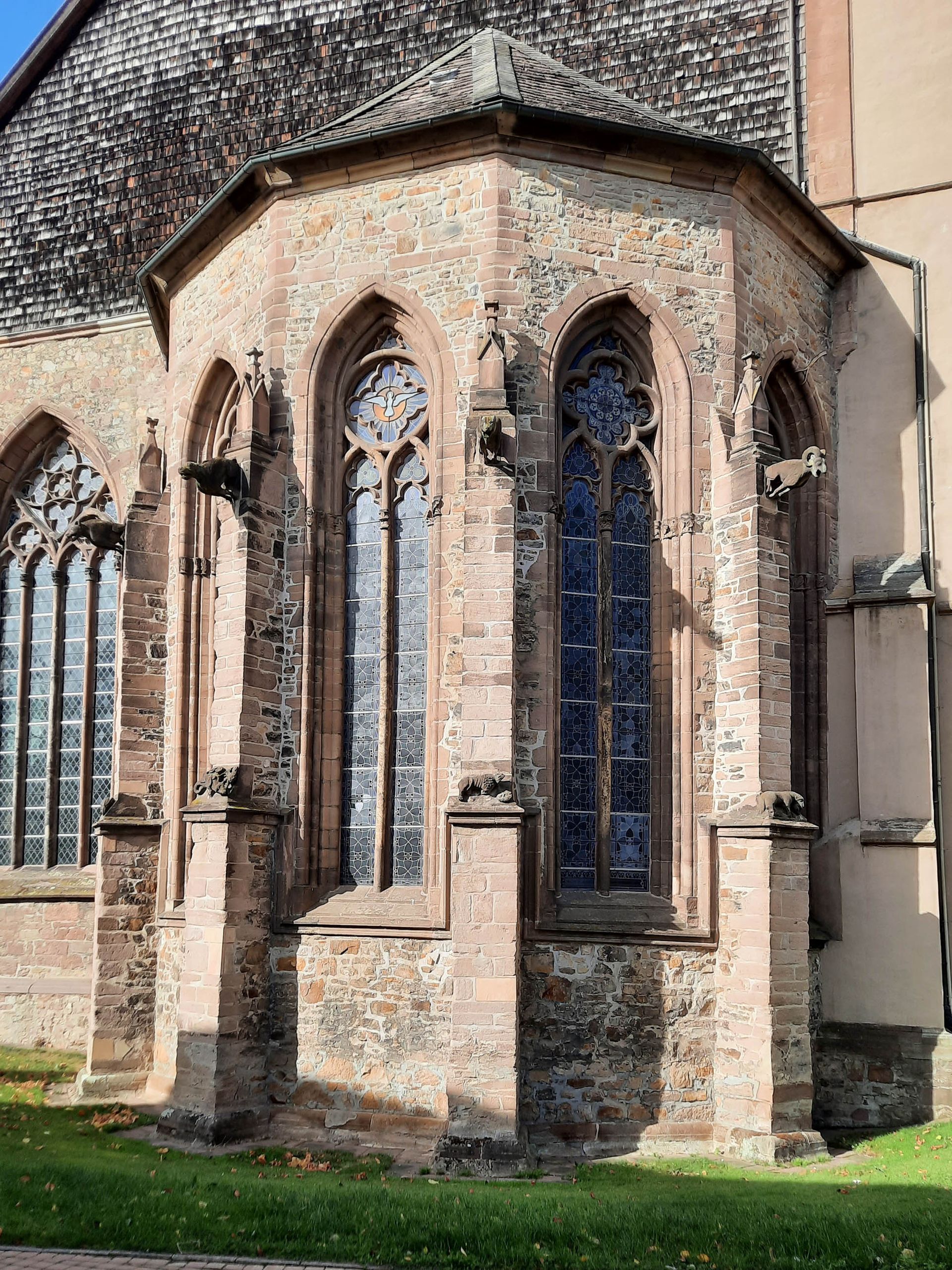 Apsis, ein runder Vorsprung an der Fassade einer Kirche. Zwischen hohen Fenstern sind Pfeiler mit steinernen Tierfiguren.