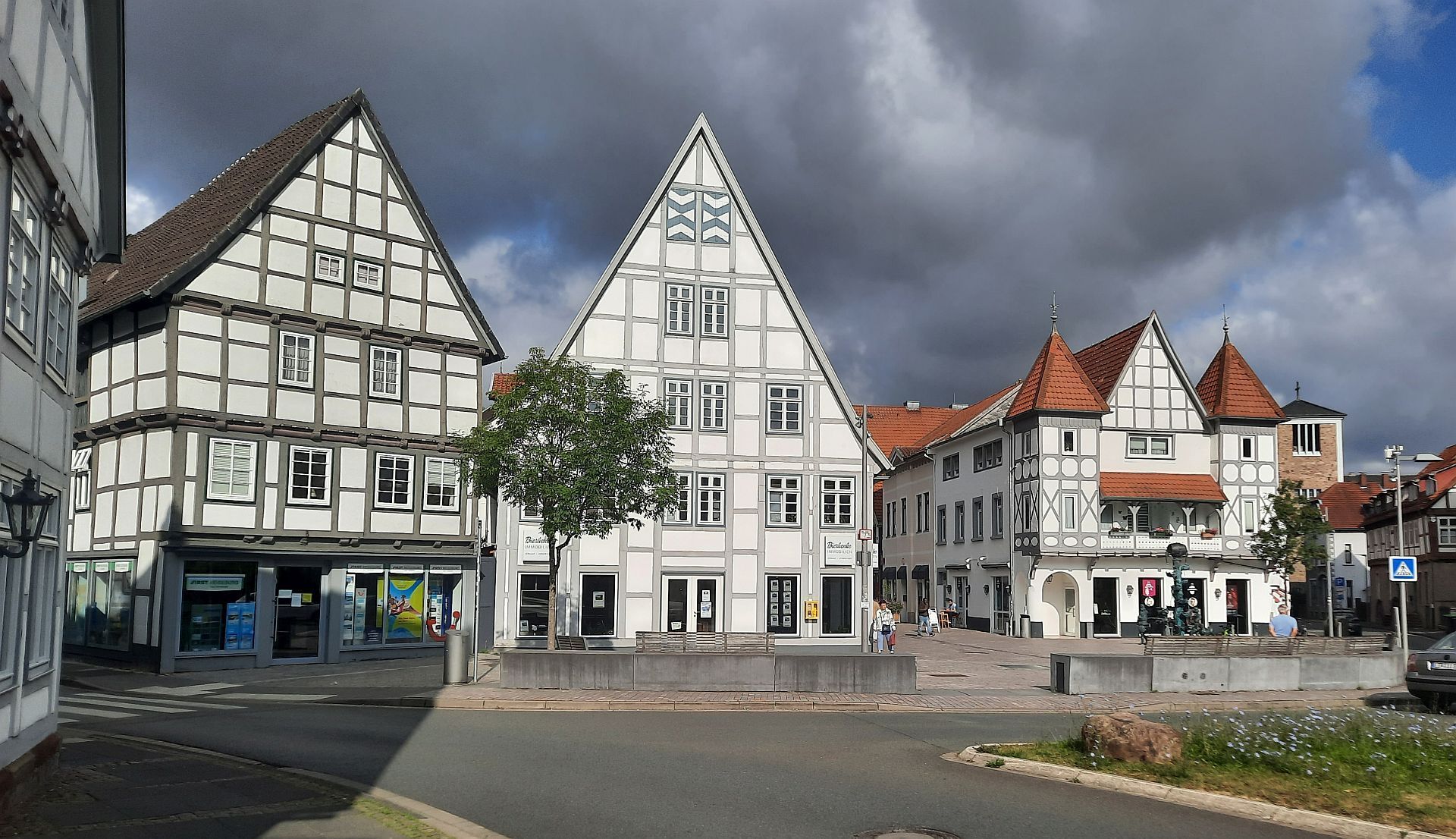 Drei Fachwerkgiebel im Sonnenlicht vor einem sommerlichen Himmel mit dunklen Wolken.