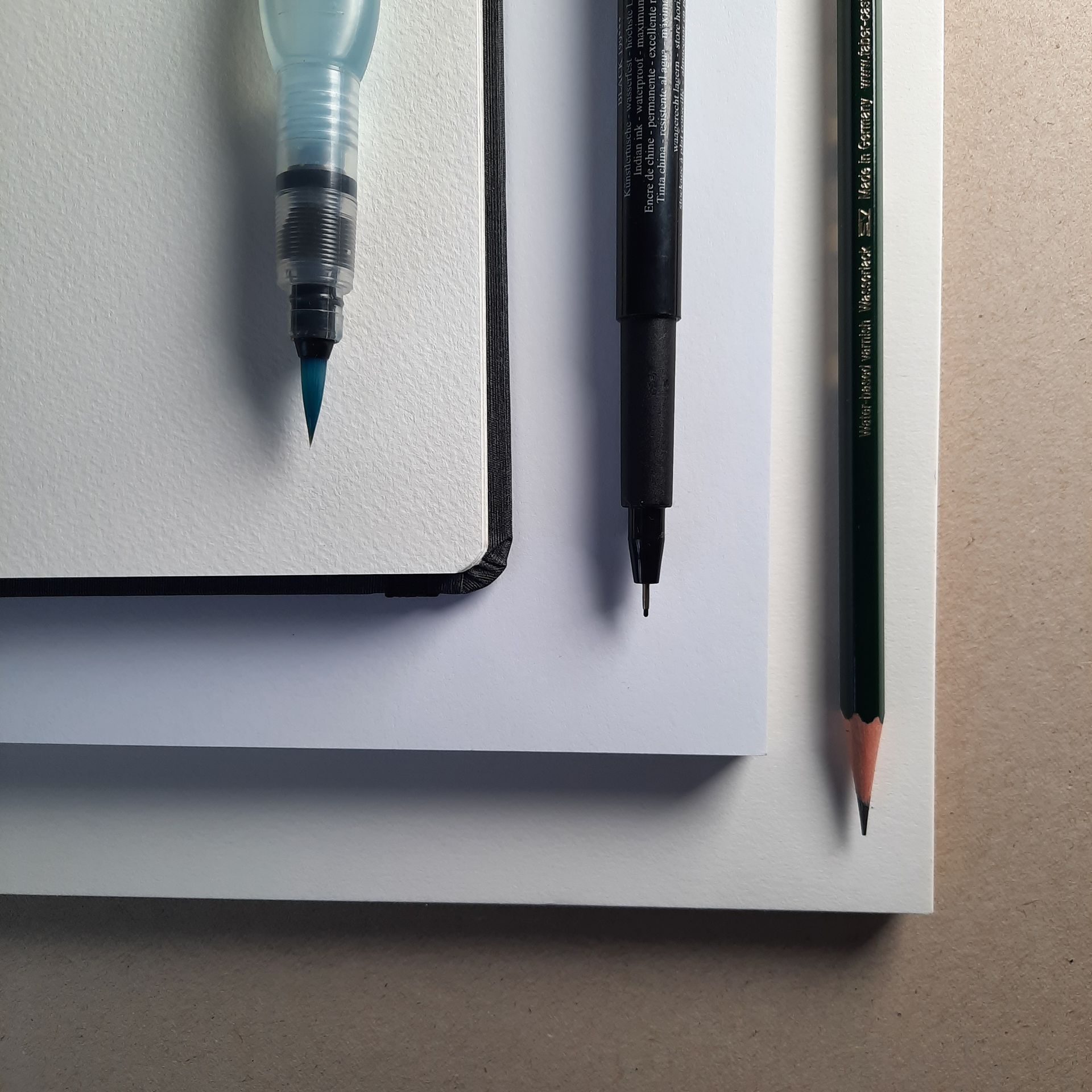 Aufsicht auf drei Papierblöcke für Aquarell, Filzstift und Bleistift. Darauf liegen die entsprechenden Stifte.