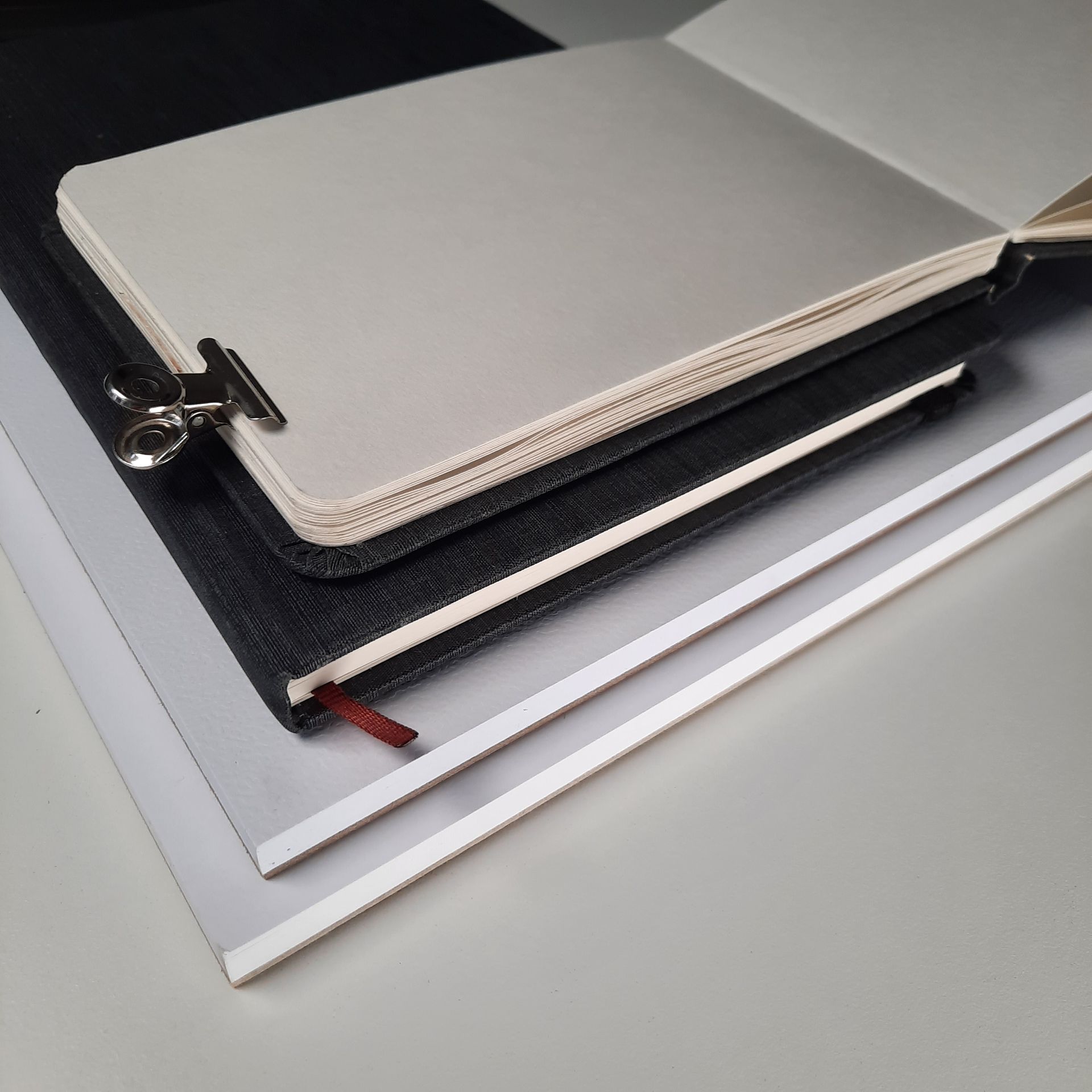 Schrägansicht von zwei Zeichenblöcken und zwei Skizzenbüchern. Eines davon aufgeschlagen und mit einer Metallklammer fixiert.