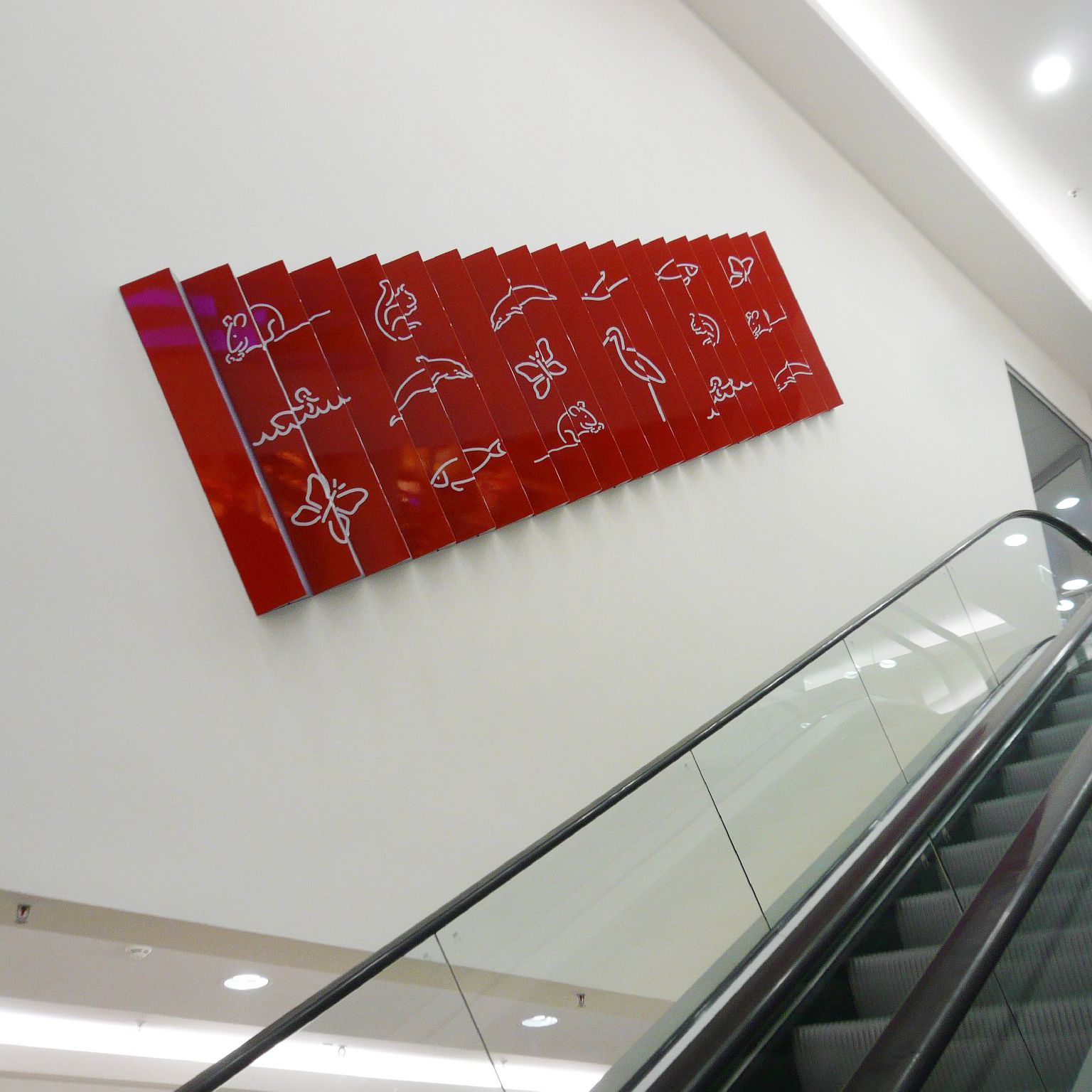 Plastisches Wandbild als Leporello neben einer Rolltreppe. Als Hintergrundfarben wechseln sich Rot und Blau ab, die Tierfiguren sind weiß.