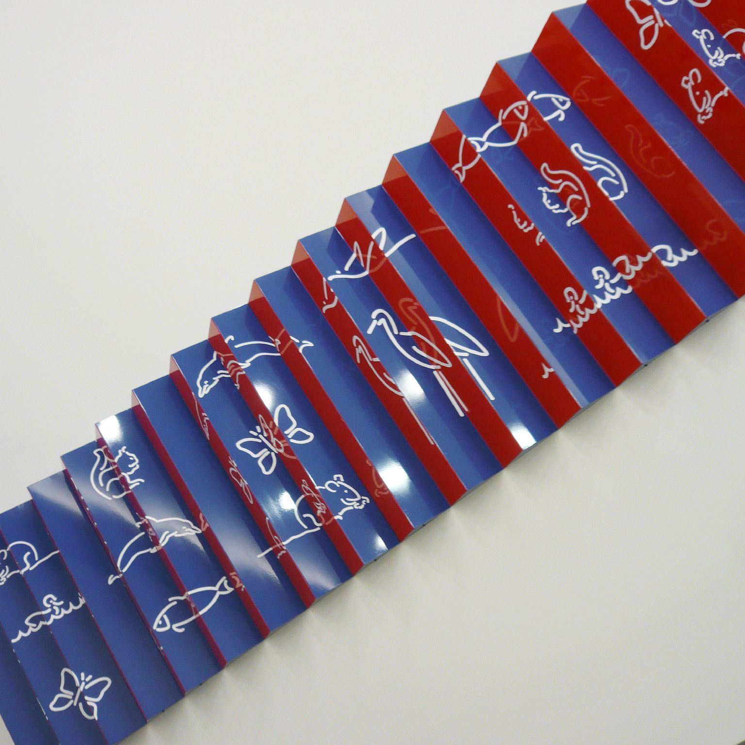 Teilausschnitt eines plastischen Wandbildes. Ein Leporello mit den Hintergrundfarben blau und rot.