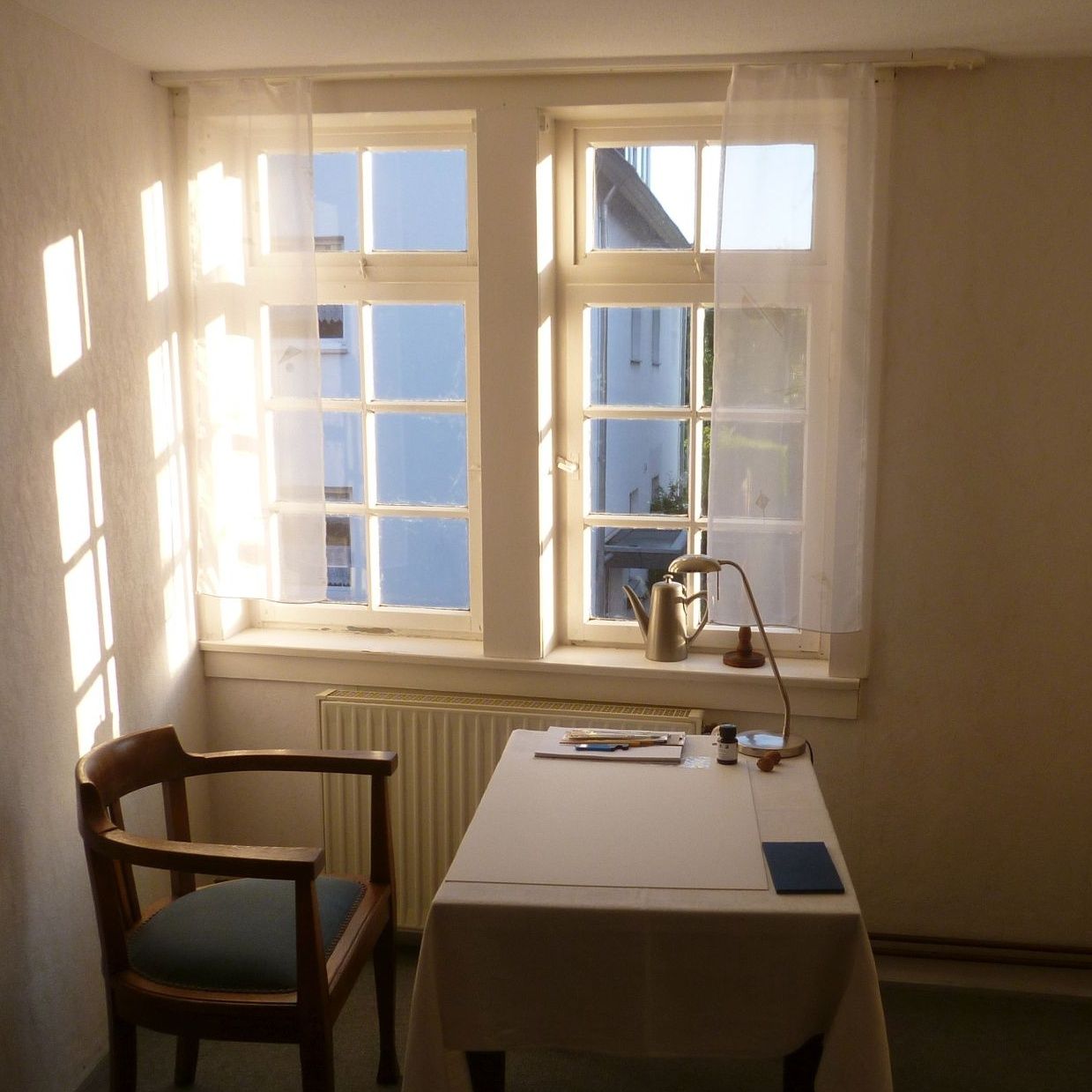 Schreibtisch und Lehnstuhl in einem kleinen Zimmer mit Sprossenfenstern.