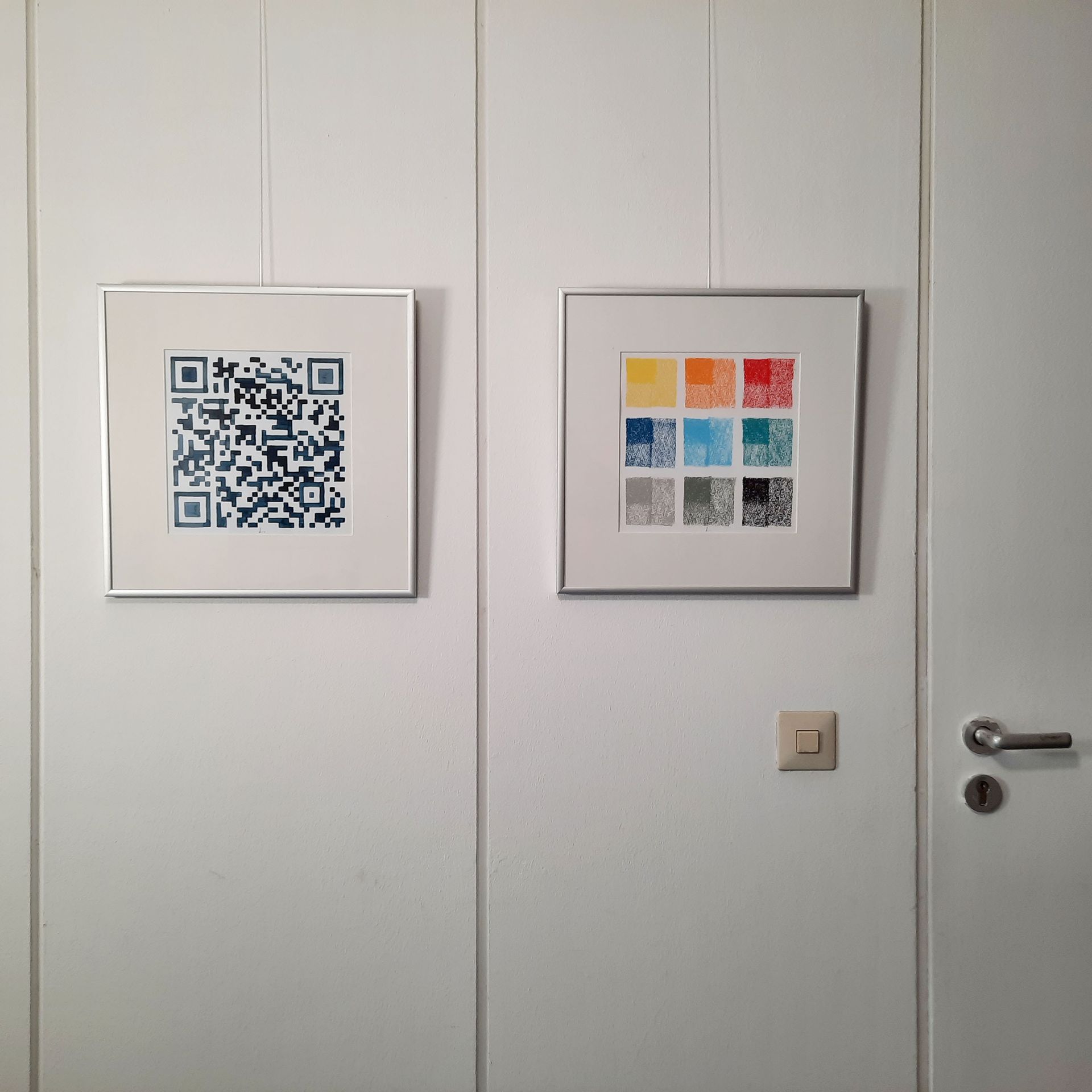 An einer weißen Bürowand hängen zwei quadratische Bilder mit Alurahmen und Passepartout. Links ein QR-Code, rechts 9 Quadrate