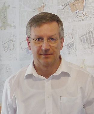 Selbstportrait vor einer Wand mit Architekturskizzen.