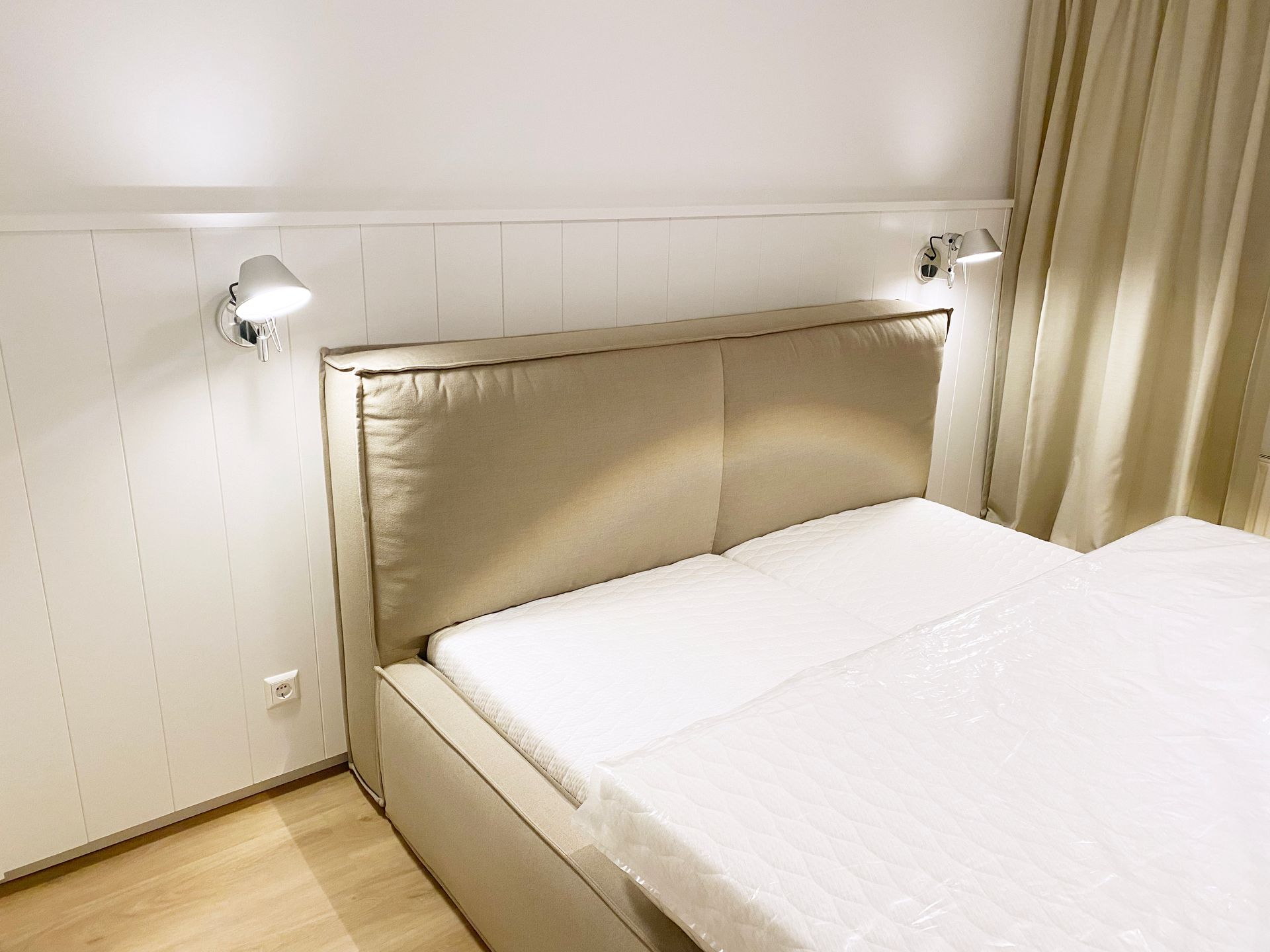 Schlafzimmer mit Boxspringbett, halbhoher Wandverkleidung, Steckdosen, Strahlern und hellen Wandpaneelen.