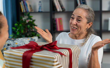 Frau lächelt und öffnet drinnen eine mit einer roten Schleife verzierte Geschenkbox.