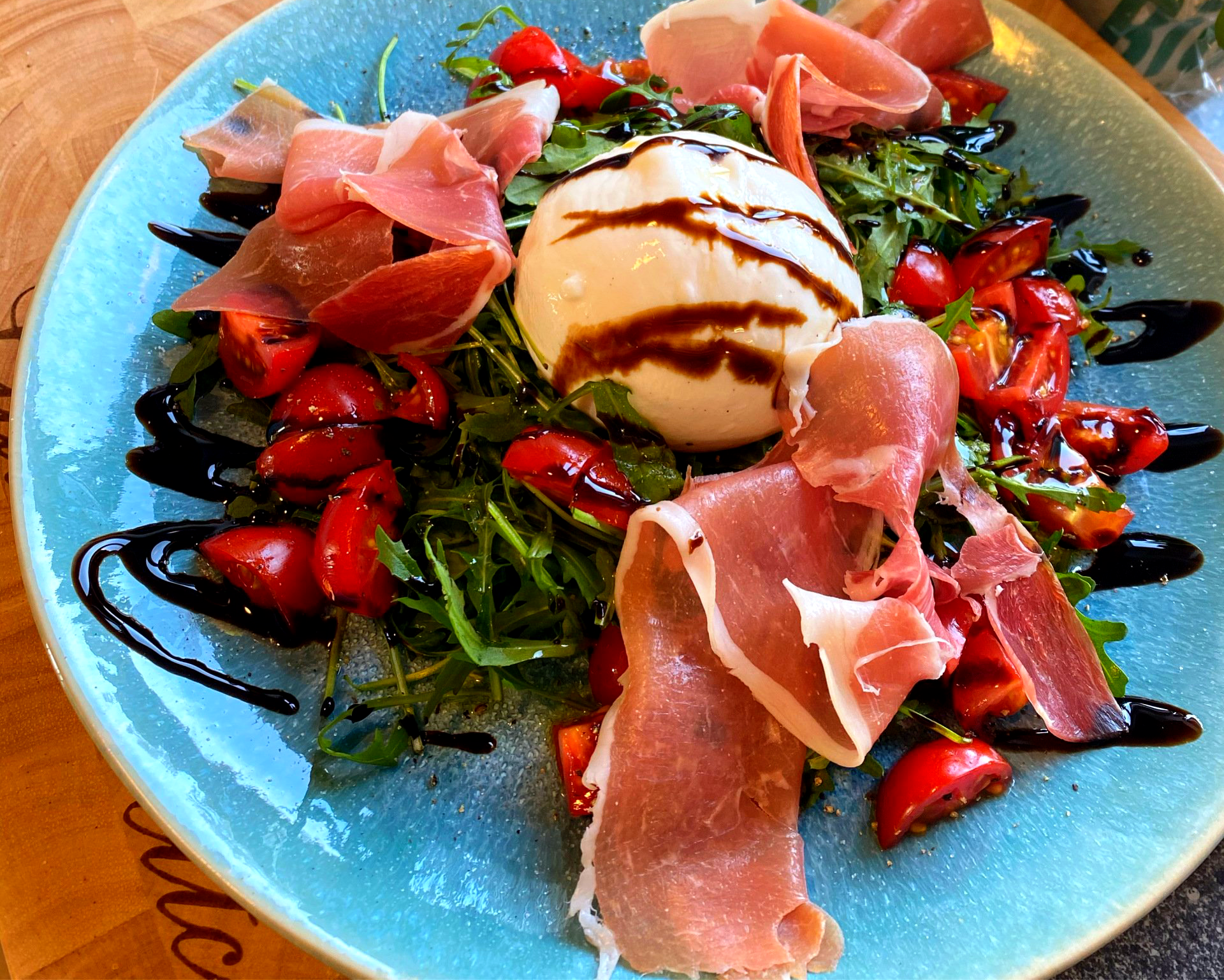 Saftige Burrata & lufgetrocknetem San Daniele Schinken (24 Monate gereift) auf knackig frischem Rucola mit sonnigen Cocktailtomaten & cremigem Balsamico
