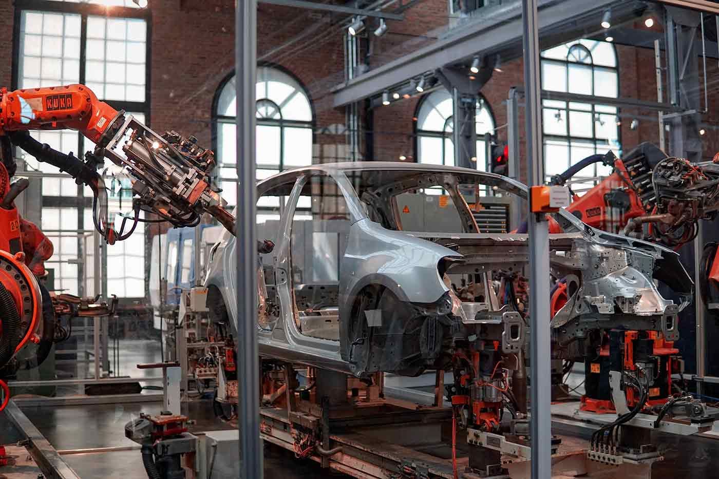 Roboterarme schweißen in einer Fabrikhalle mit Backsteinwänden und Bogenfenstern eine Autokarosserie.