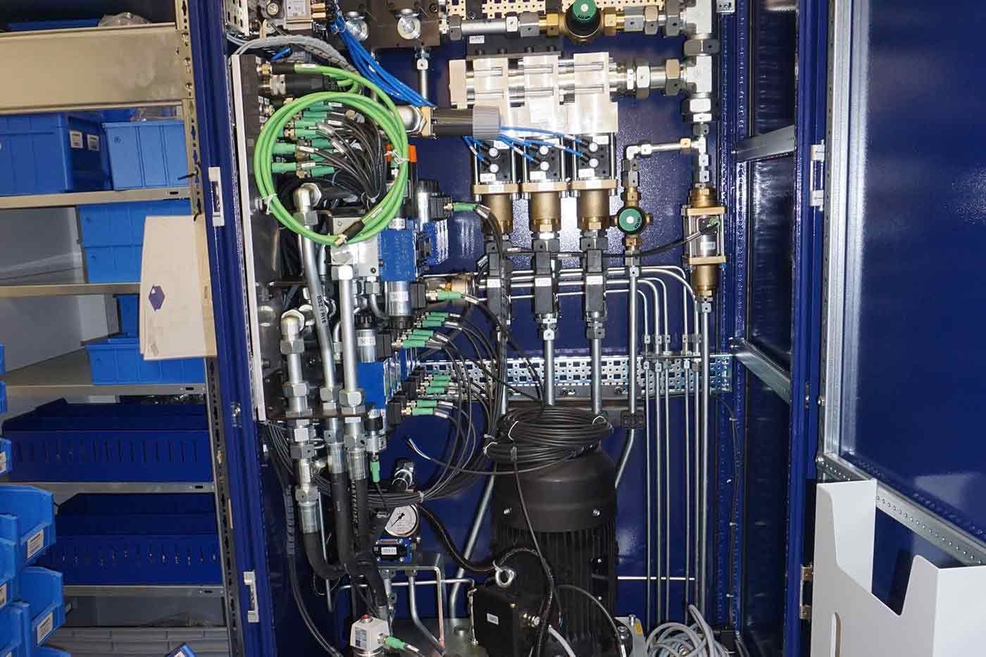 Innenraum eines blauen Metallschranks mit komplexen Maschinen und Rohrleitungen. Grüne, schwarze und silberne Komponenten.