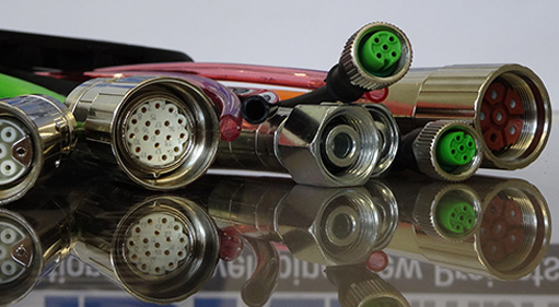 Nahaufnahme verschiedener runder elektrischer Steckverbinder mit mehreren Pins, die sich auf einer Oberfläche spiegeln.