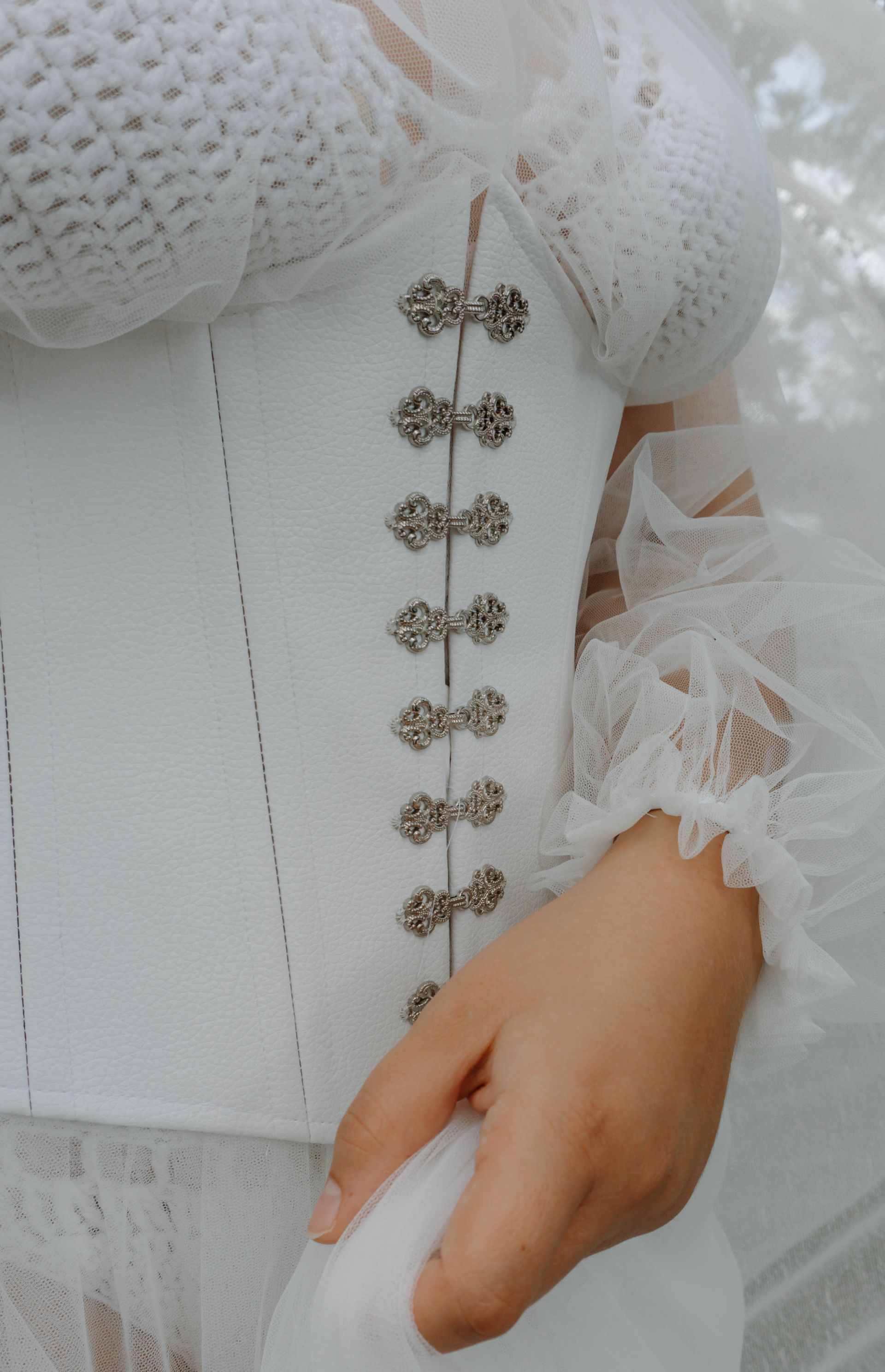 Detailaufnahme eines handgefertigten Outfits von Katyliz - Frau trägt weiße Corsage mit Zierverschlüssen