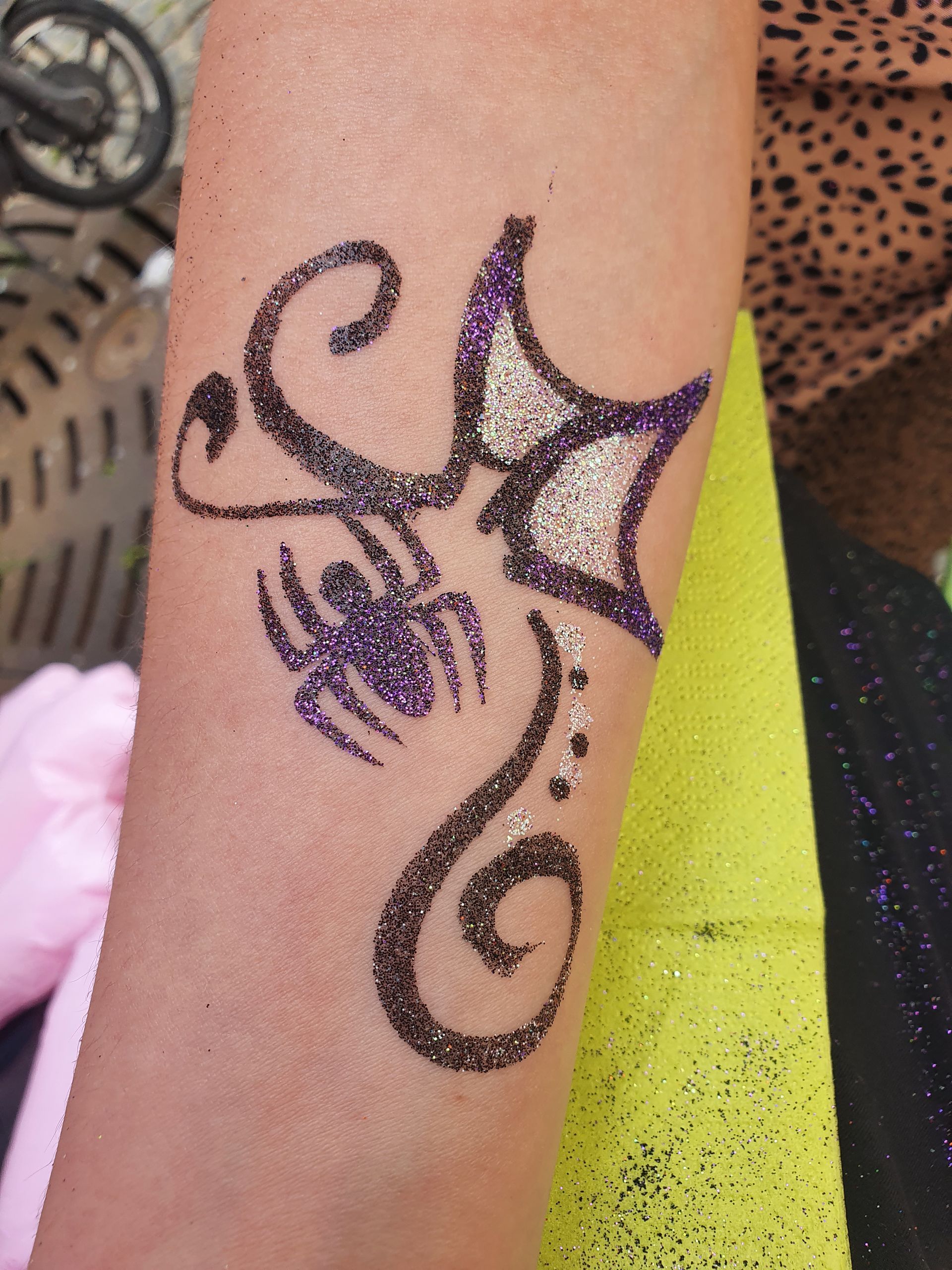 Arm mit schwarz-violettem Glitzer-Körperbemalung im Tribal-Stil auf der Haut neben einem neongelben Tuch