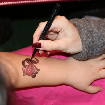 Eine Hand zeichnet mit einem schwarzen Stift ein herzförmiges Muster auf den Unterarm eines Kindes.