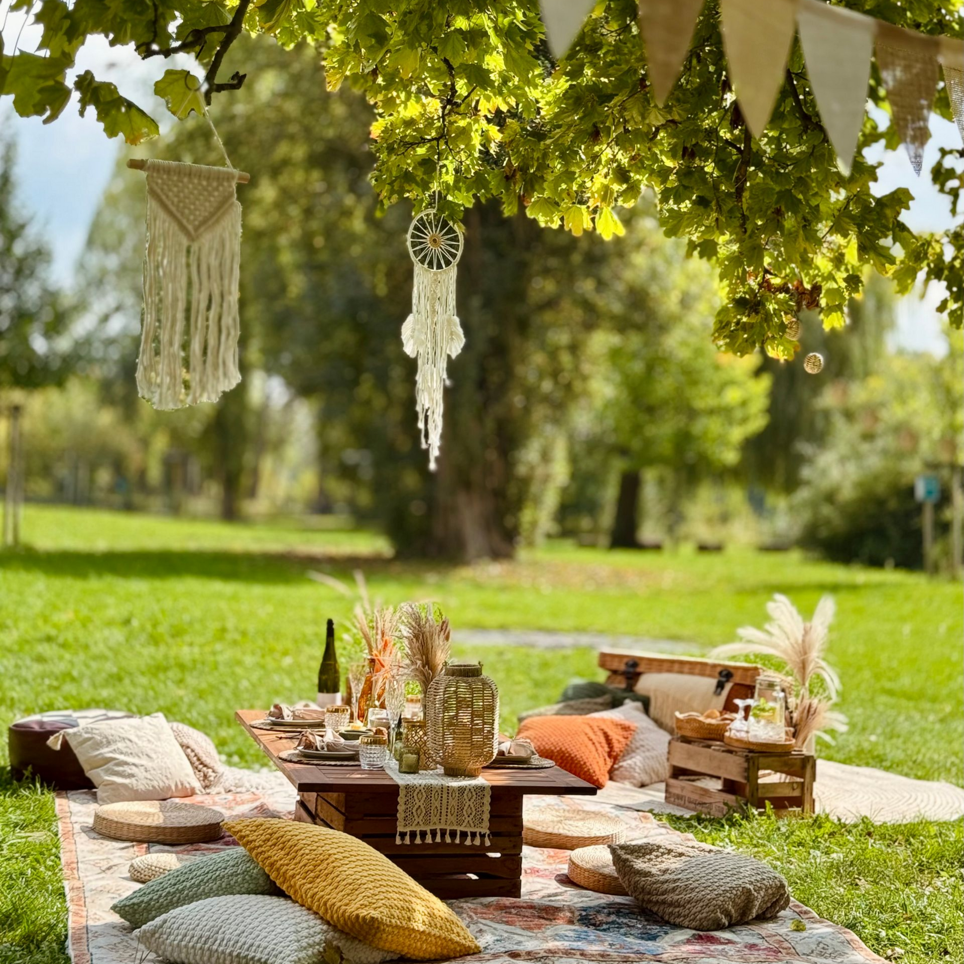 Böhmisches Picknick-Setup in einem Park mit Kissen, Teppich und Dekorationen, die von einem Baum hängen.