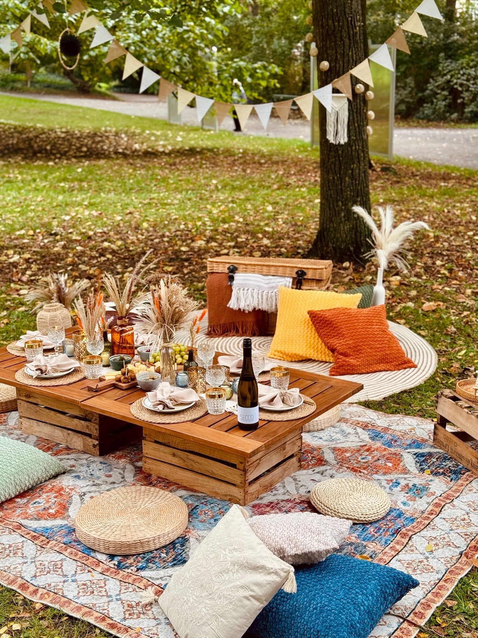 Picknick-Aufbau in einem Park mit Decken, Kissen, einem Holztisch und Dekorationen.