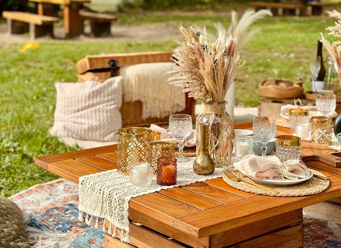 Picknick-Aufbau: Holztisch mit Dekorationen, darunter Blumen und Gläser, auf Gras im Freien.