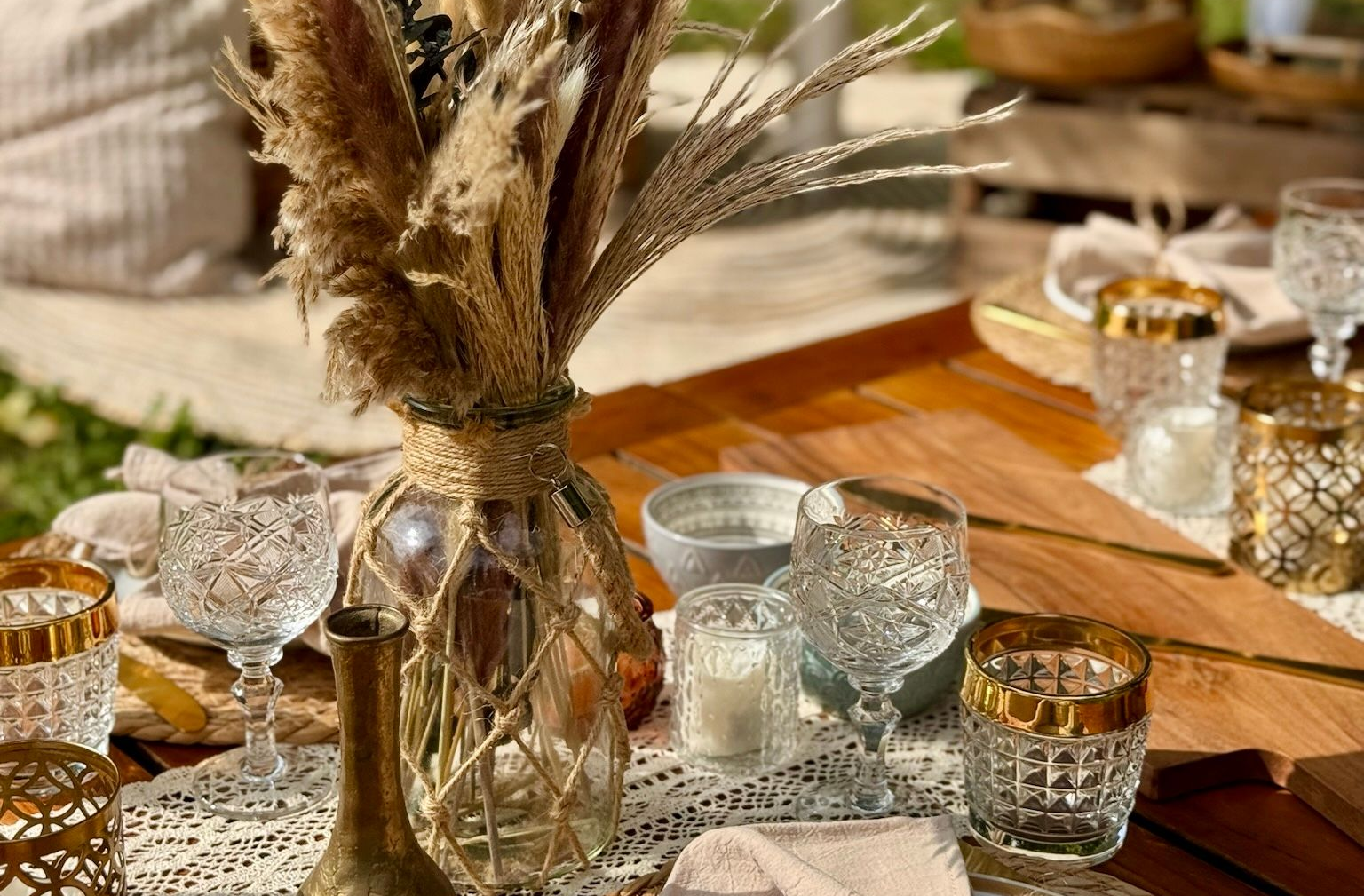 Picknicktisch mit Blumenstrauß, Glaswaren, Kerzen und beigem Dekor.