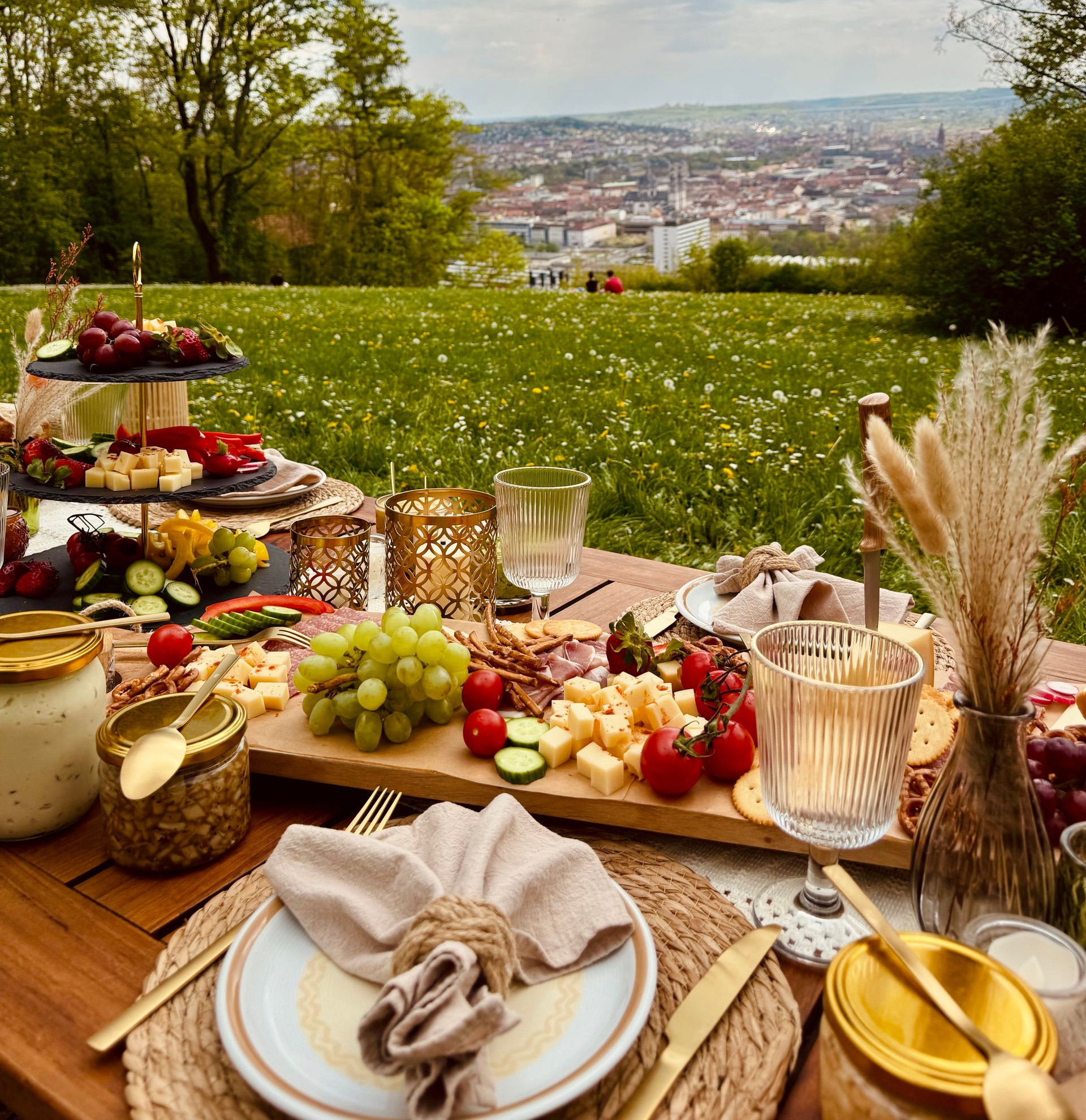 Tischdekoration im Freien mit Käse, Trauben, Oliven und Blumengestecken.