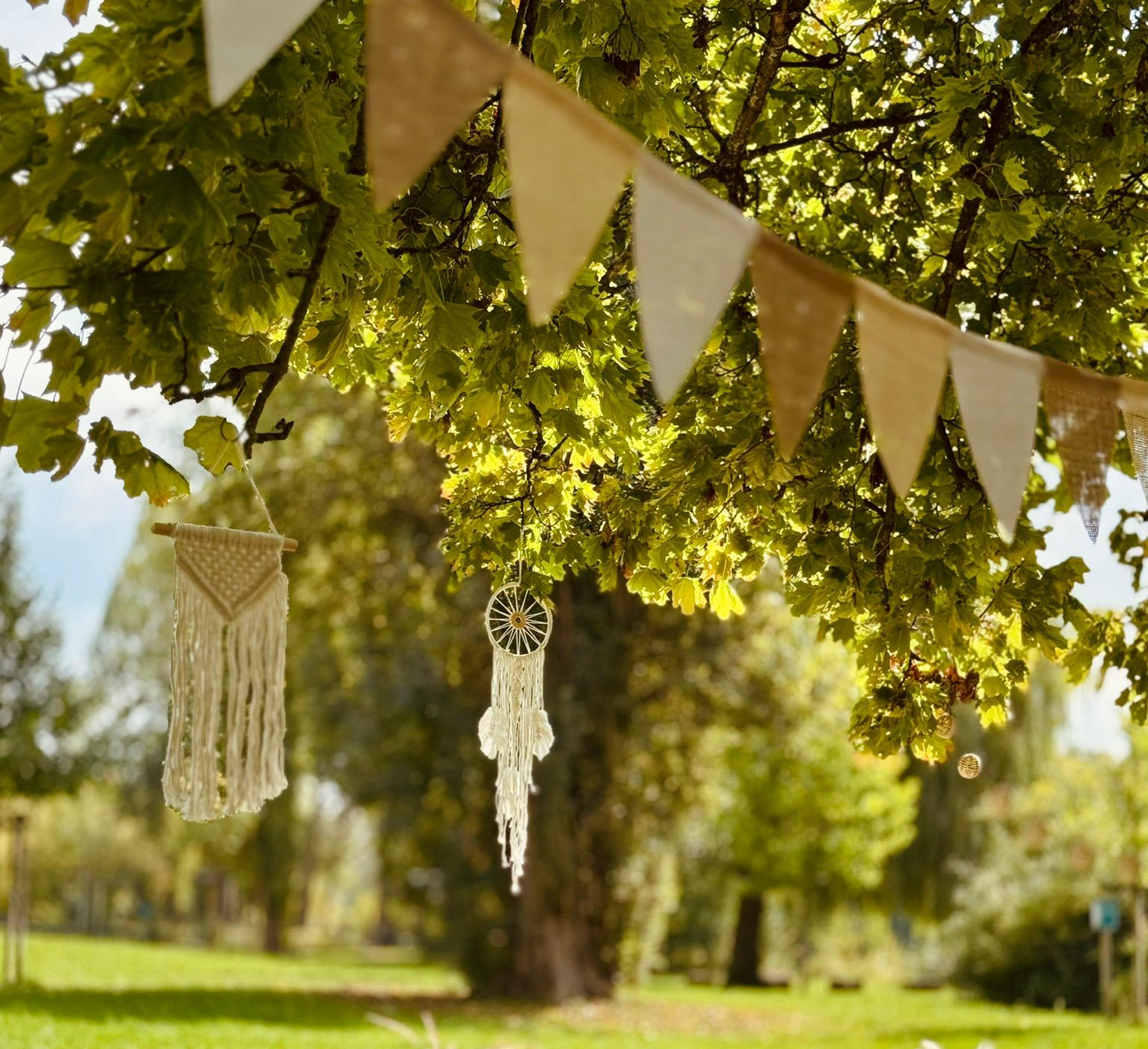Wimpel und Makramee hängen von den Ästen in einem sonnigen Park.